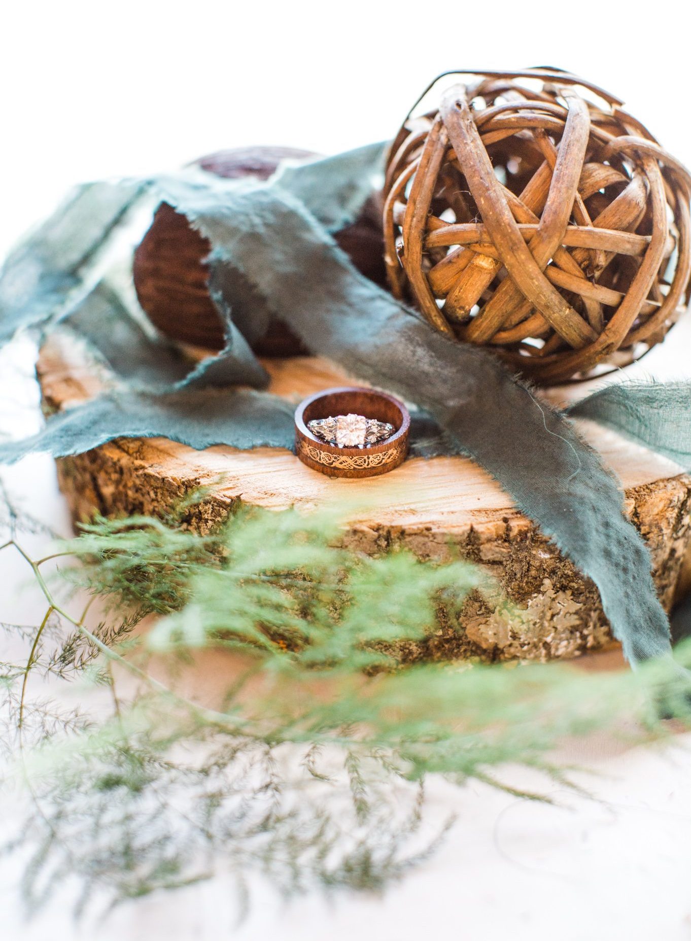 Wedding rings on wood slab with green ribbon and greenery