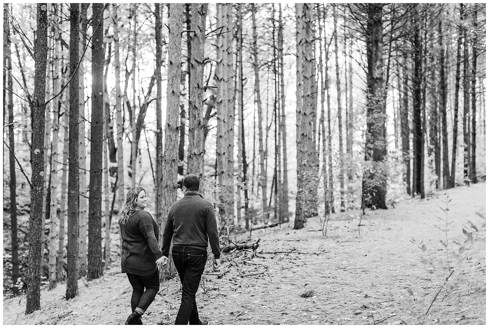 Couple walks through forest together in Northern Michigan during Traverse City Engagement session.
