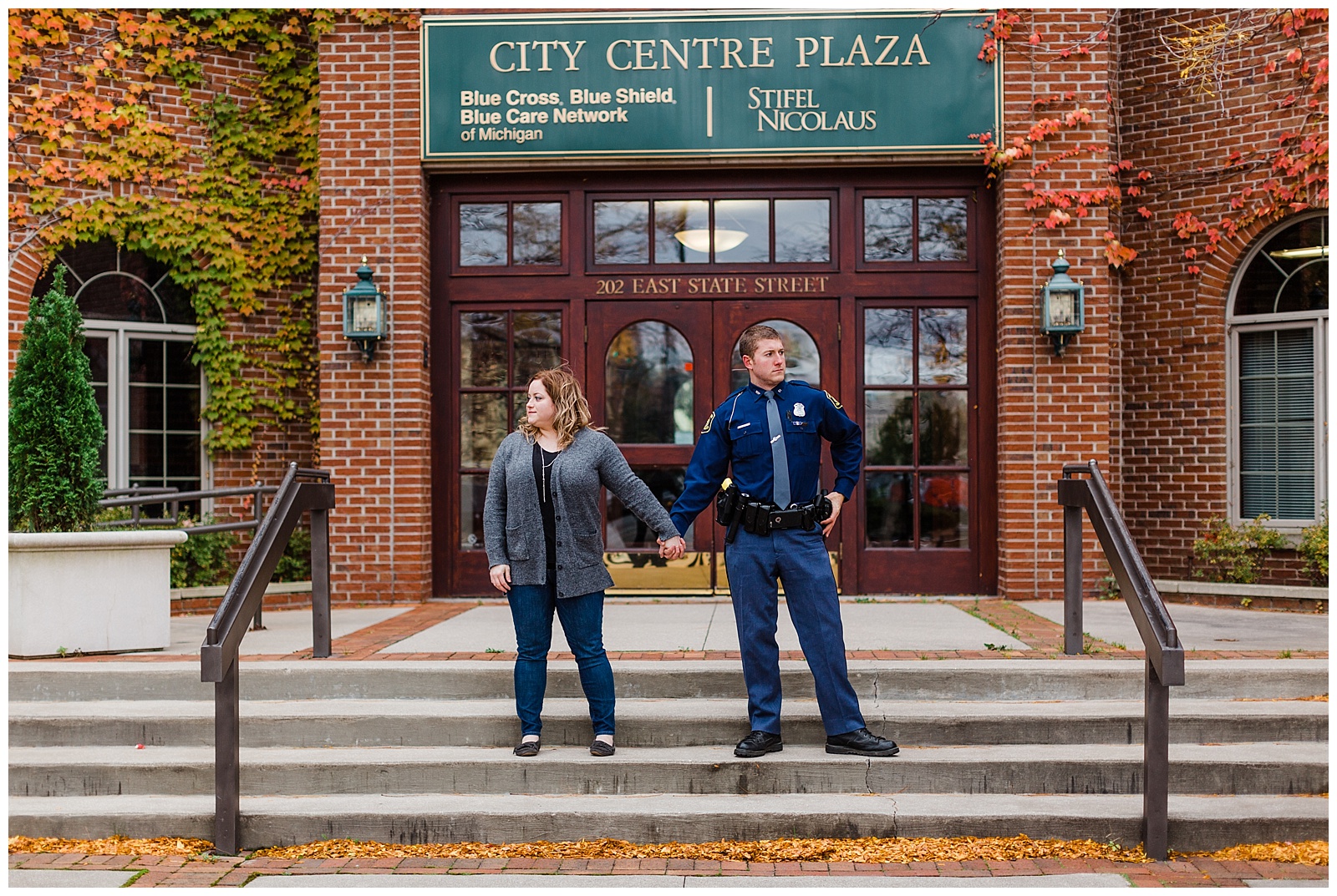 Couple looks opposite ways while holding hands in front of building downtown during Traverse City Engagement session.