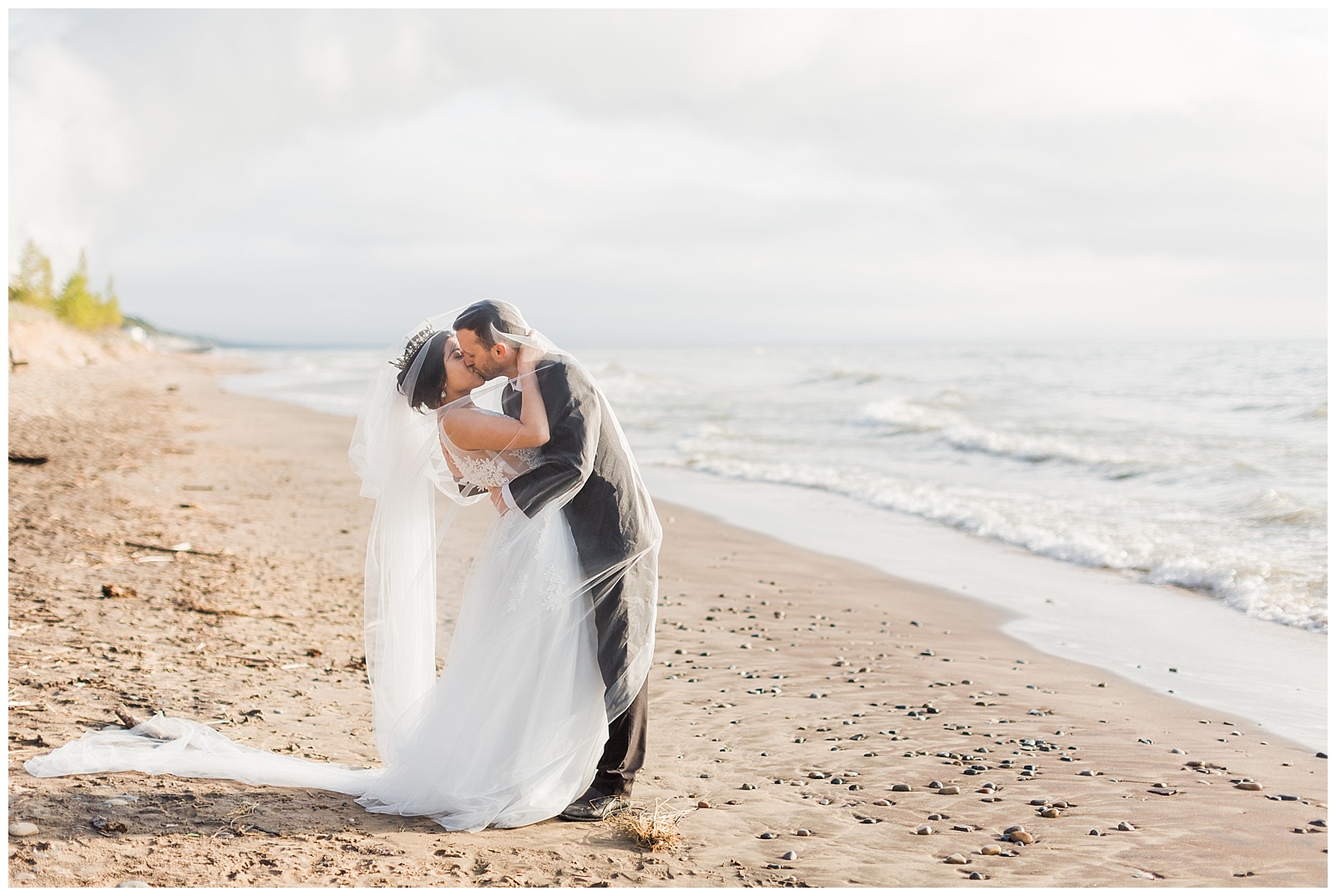 Bride and groom kiss on beach in Traverse City during Northern Michigan beach wedding.