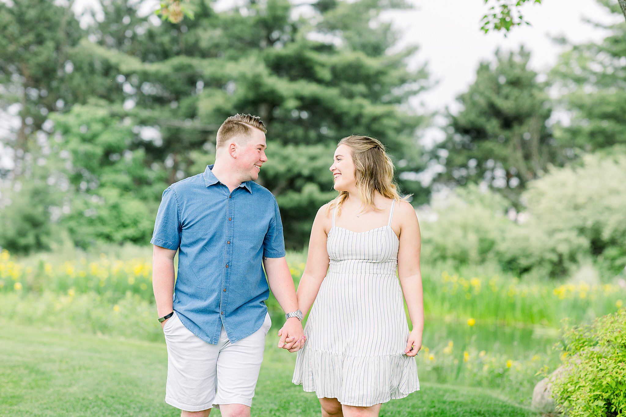 Couple walks and smiles at each other during Grand Traverse Bay engagement session photos.