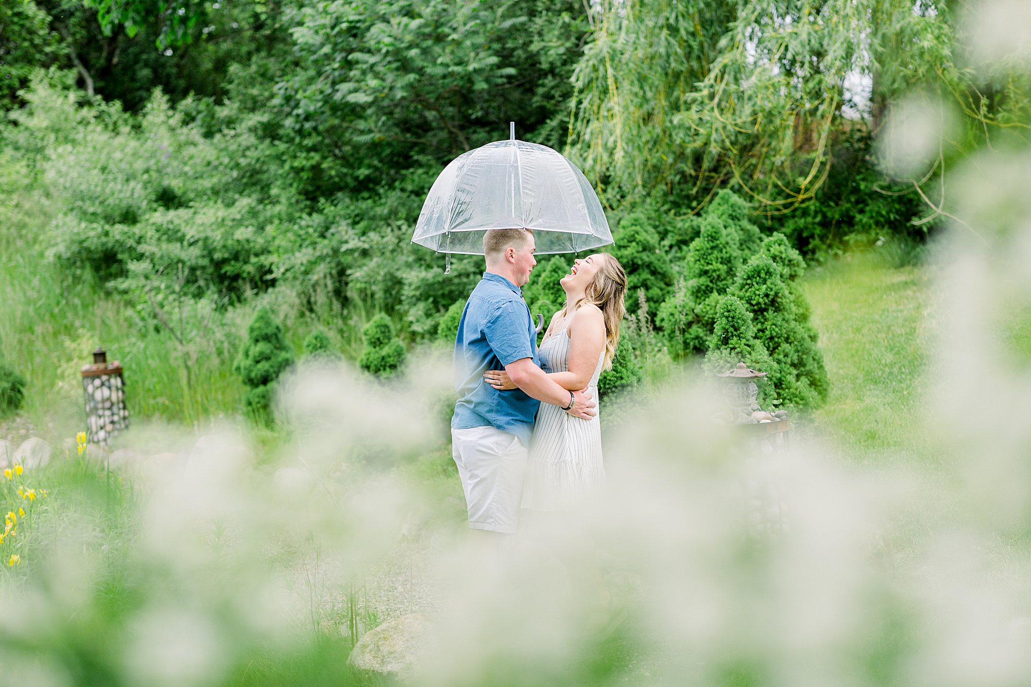 Couple laughs under umbrella during Grand Traverse Bay engagement session.