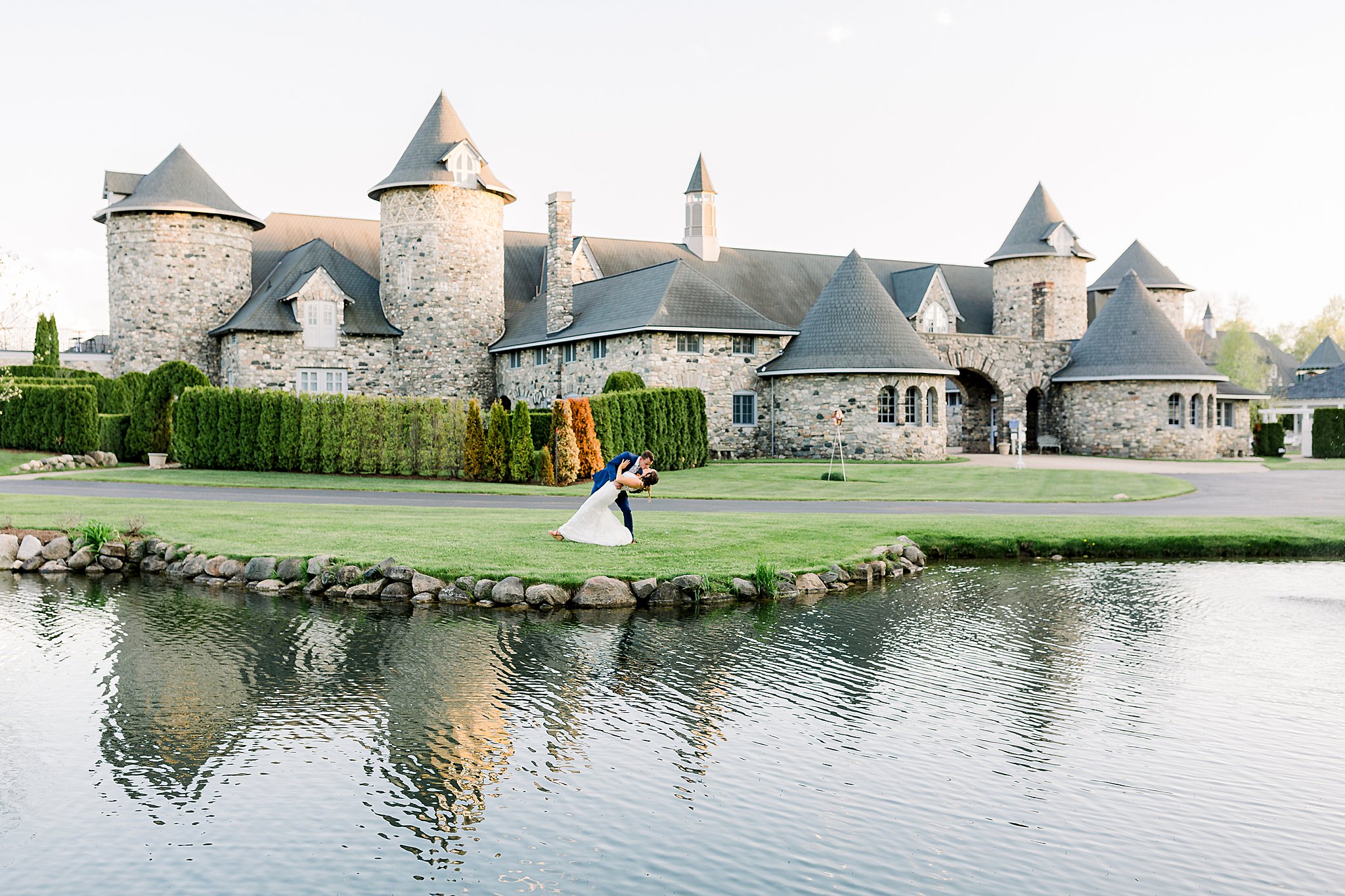 Groom dips bride and kisses her in front of Castle Farms lake during Spring Castle Farms wedding.