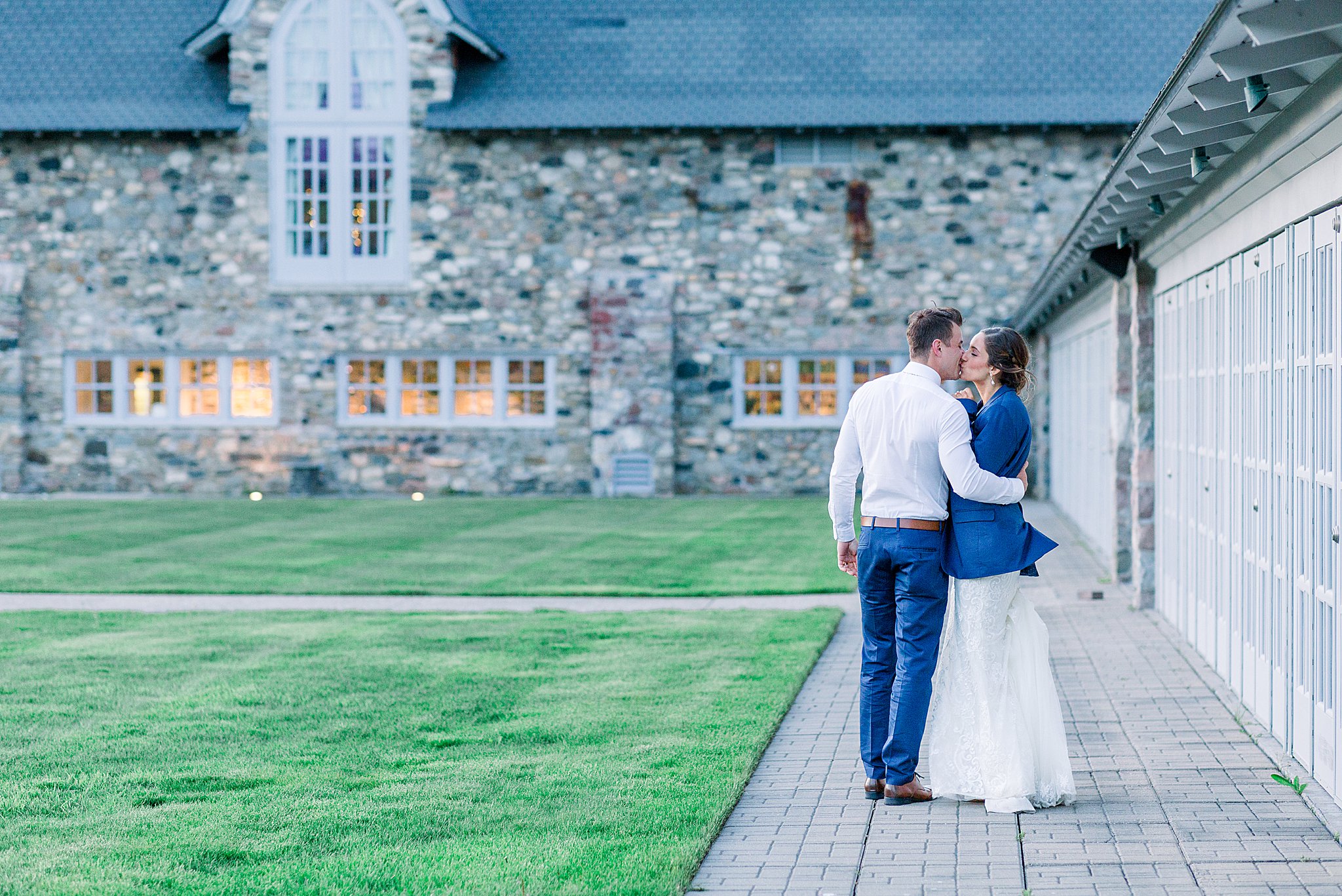 Groom wraps bride in jacket and kisses her at dusk during Spring Castle Farms wedding.