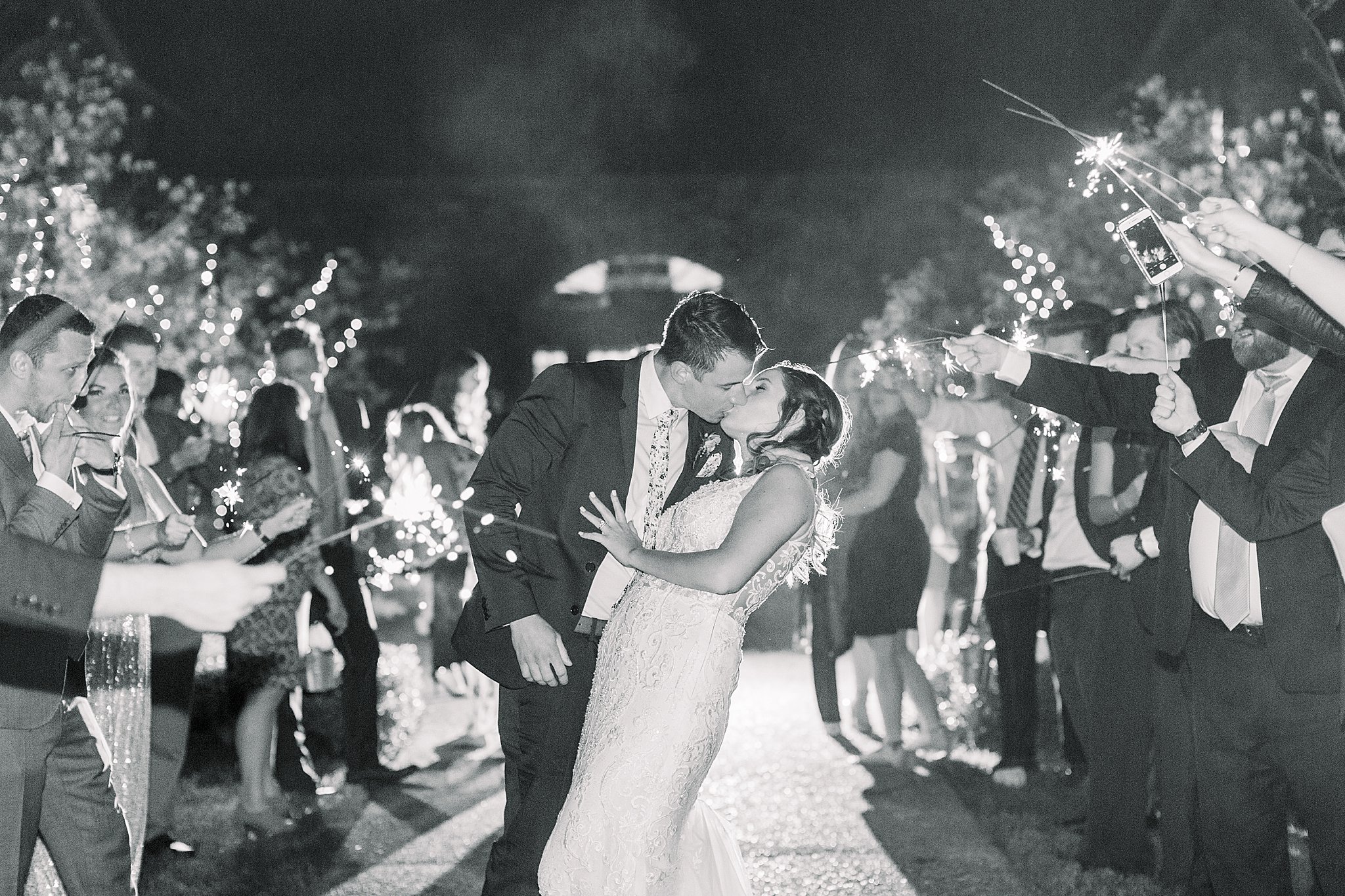 Black and white image of groom dipping bride and kissing her during sparkler exit at spring Castle Farms wedding.