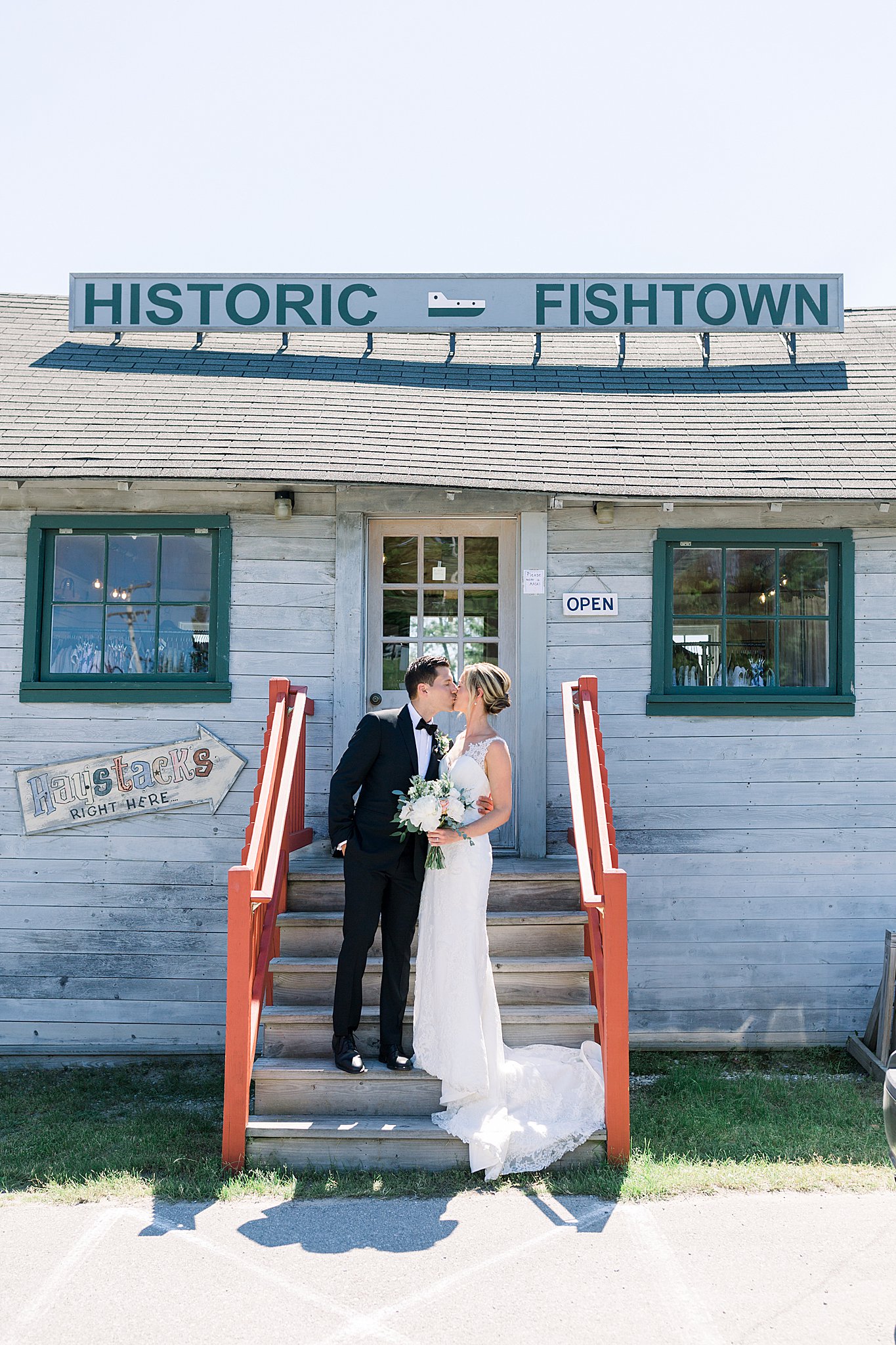 Bride and groom kiss under Historic Fishtown sign during intimate Lake Michigan wedding in Leland, Michigan.