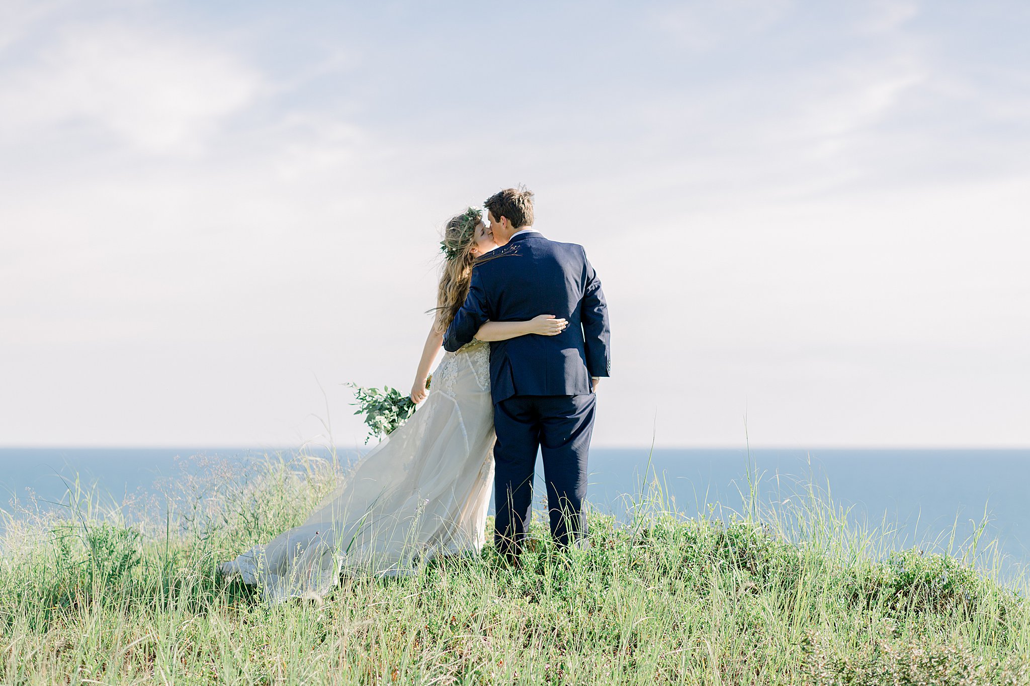 Bride and groom kiss on sand dunes overlooking Lake Michigan during Northern Michigan elopement in Frankfort, Michigan.