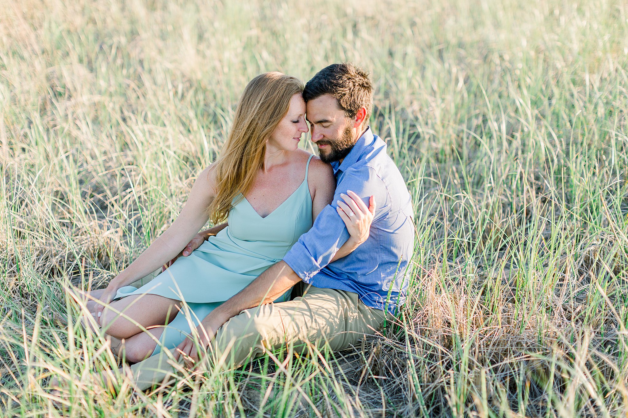 Couple snuggles in grass during Peterson Beach Sleeping Bear Dunes engagement session.