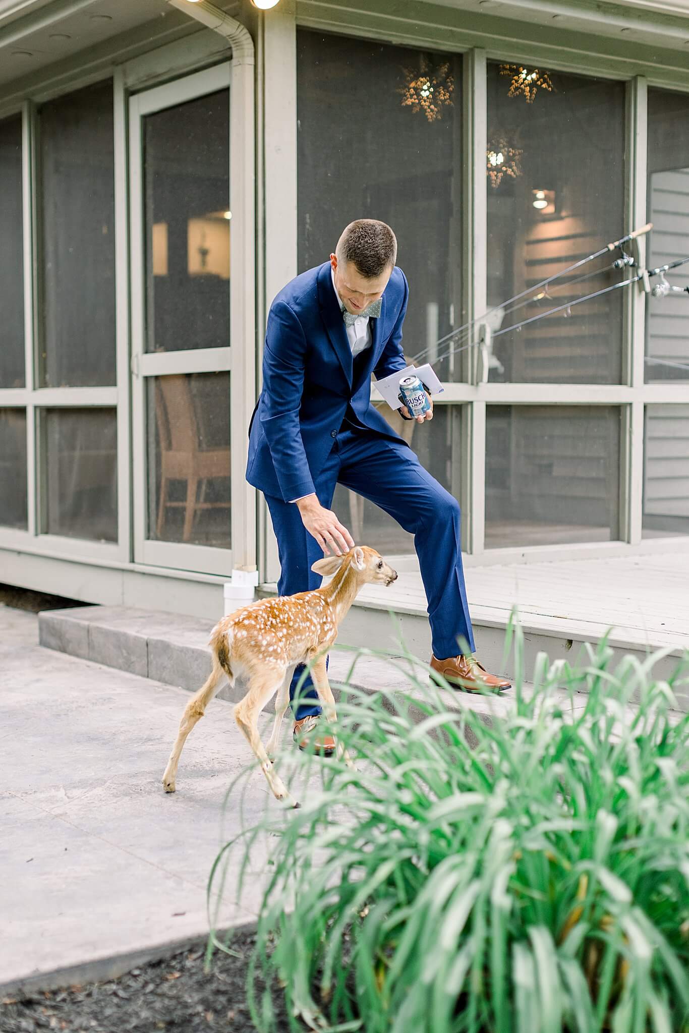 Groom pets baby deer during summer backyard wedding in Northern Michigan.