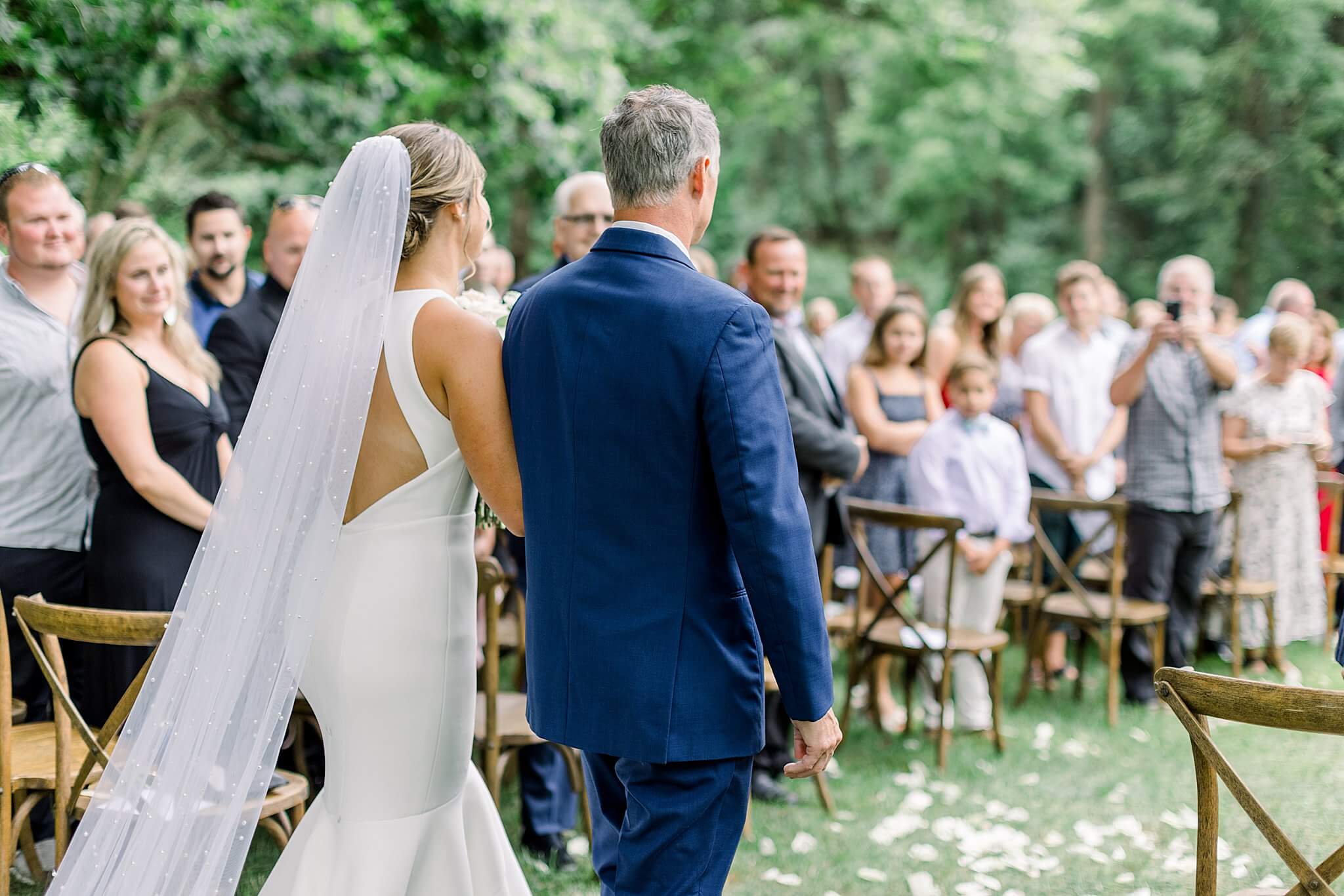 Bride walks down the aisle with her dad during summer backyard wedding in Northern Michigan.