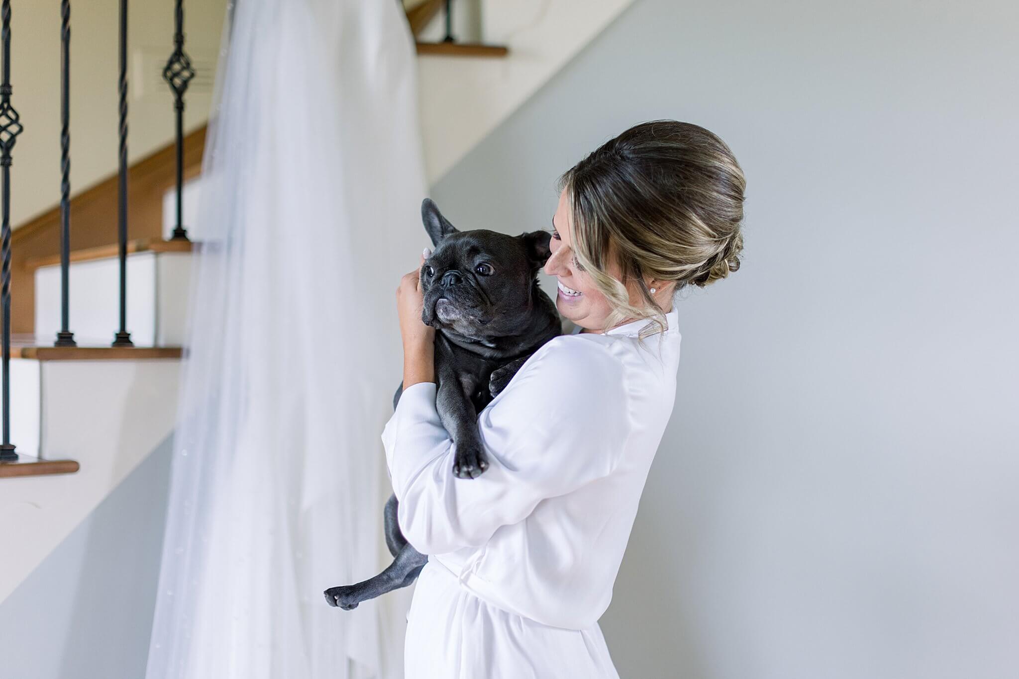 Bride hugs puppy in front of her dress while she gets ready for her summer backyard wedding in Northern Michigan.