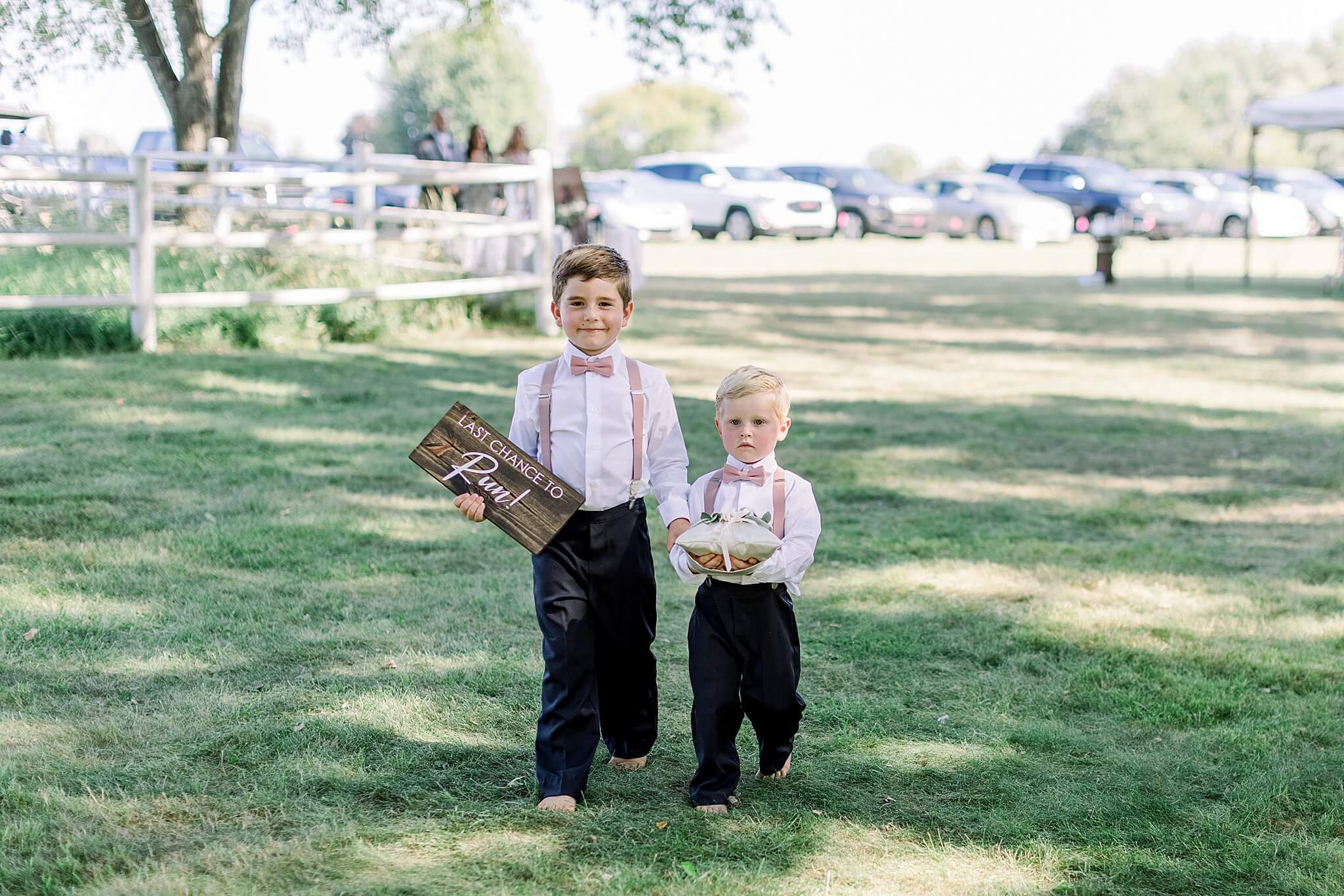 Ring bearers carry signs down aisle during Michigan Summer Backyard Wedding ceremony.