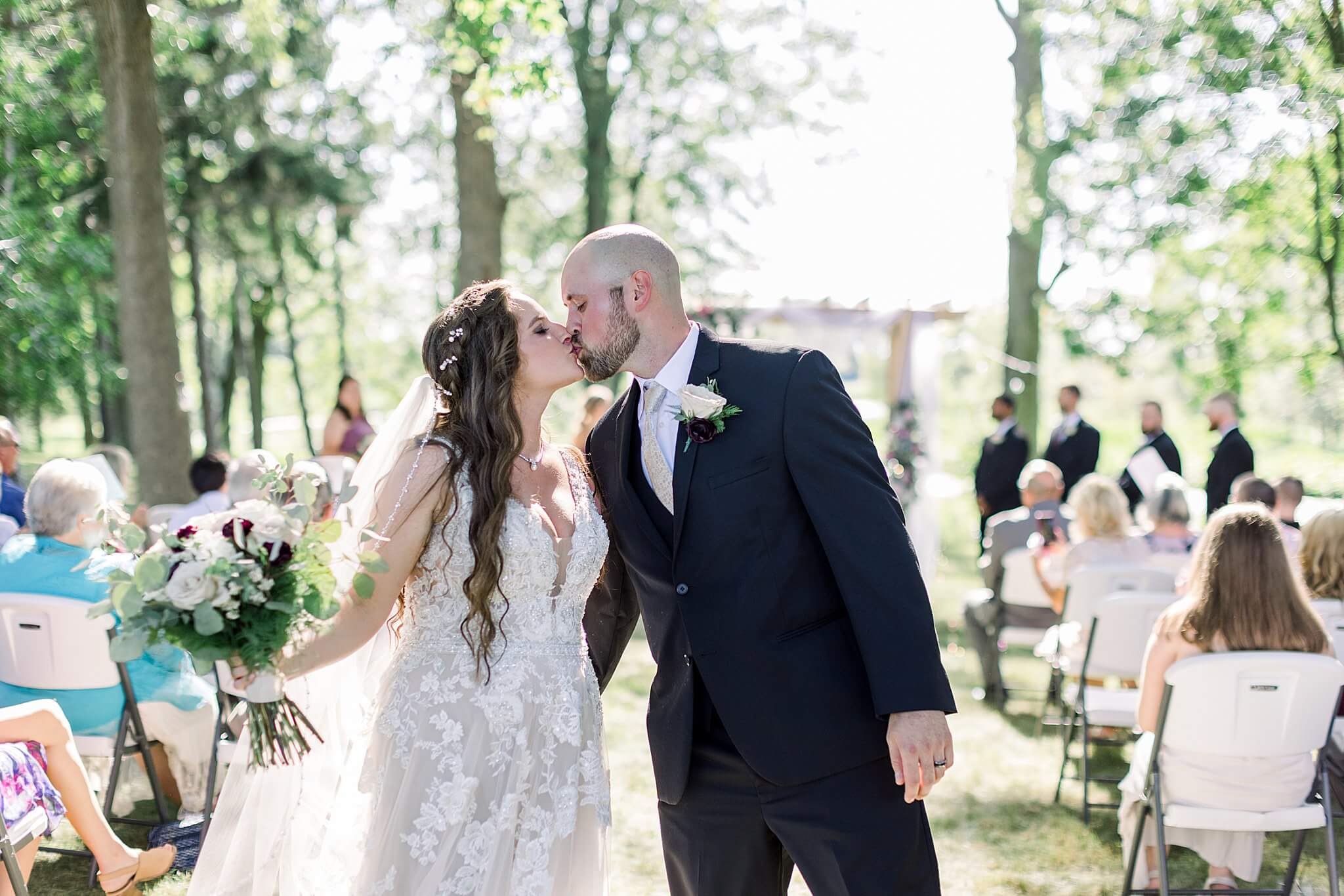 Bride and groom kiss at end of aisle during Michigan Summer Backyard Wedding