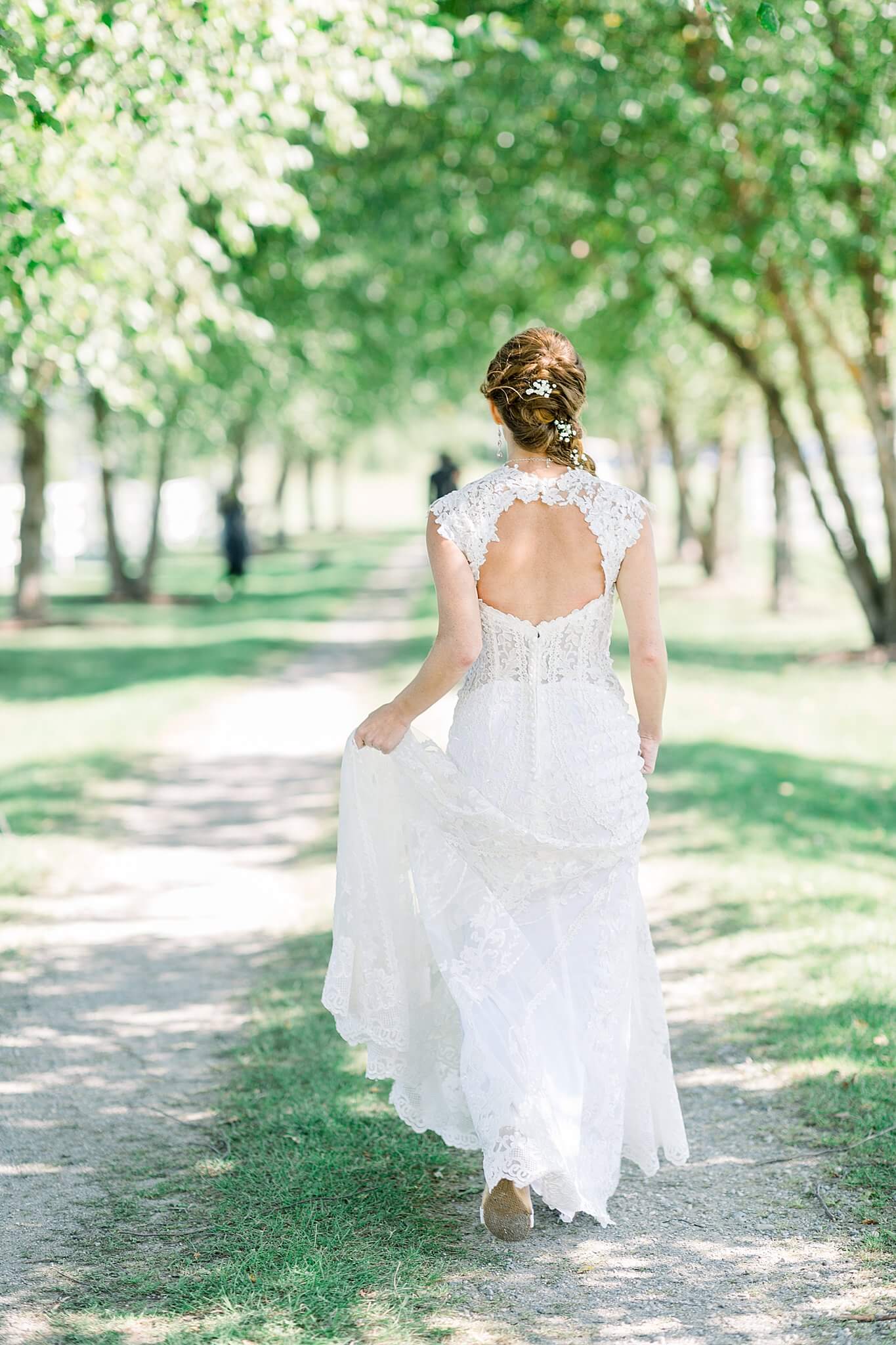 Bride walks down lane of trees for first look with groom at Crooked Creek Ranch wedding.