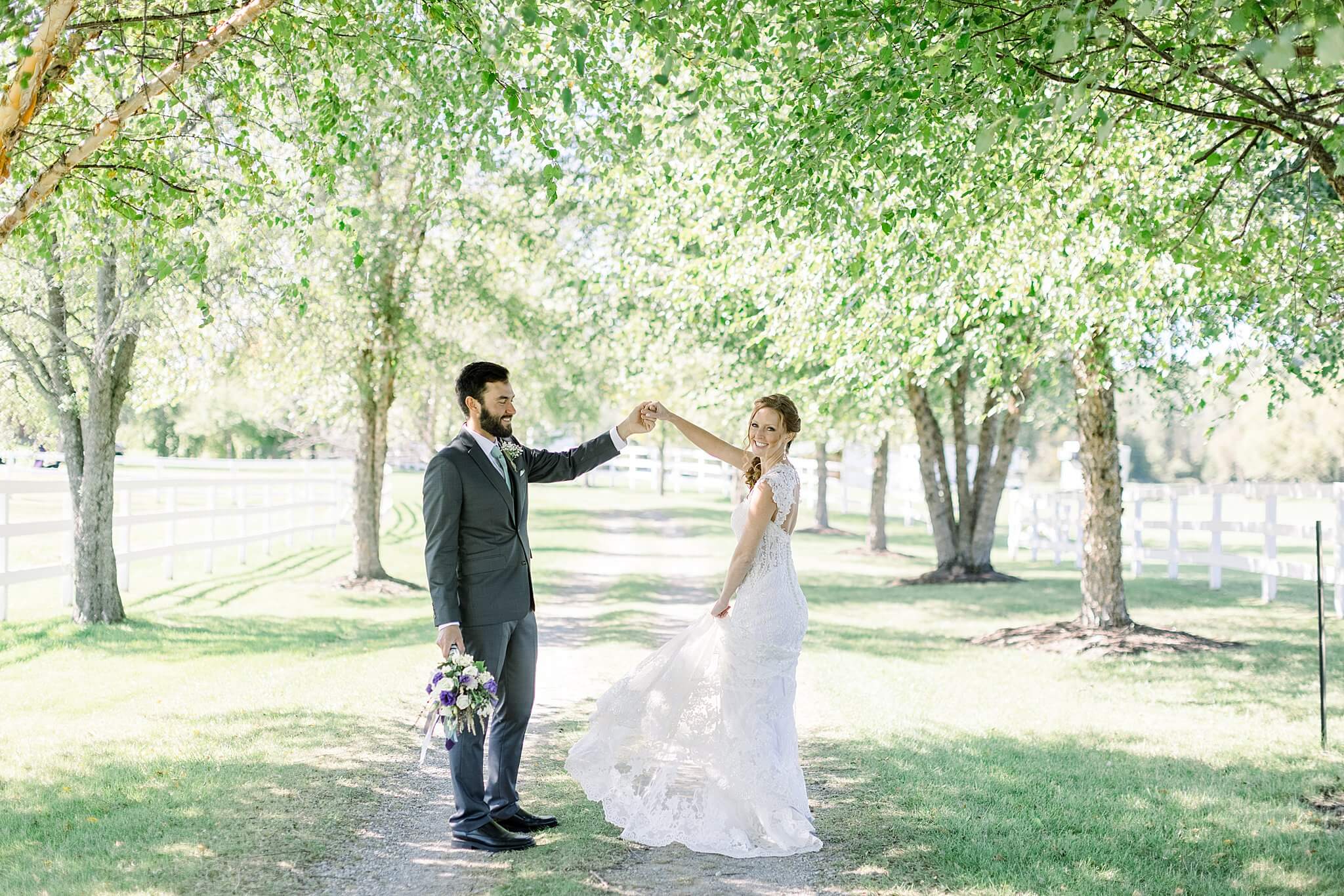 Groom twirls bride in shaded lane during Crooked Creek Ranch wedding.