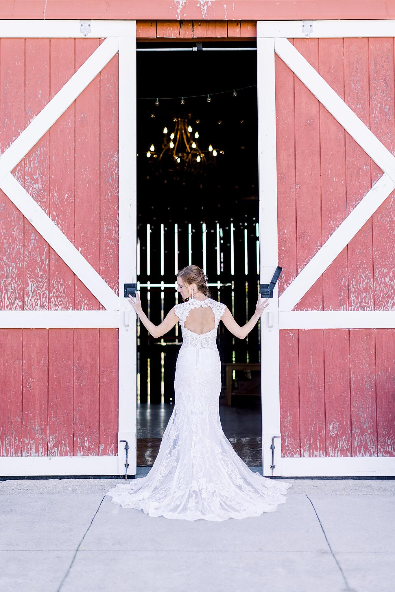 Bride poses with red barn doors at Crooked Creek Ranch wedding.