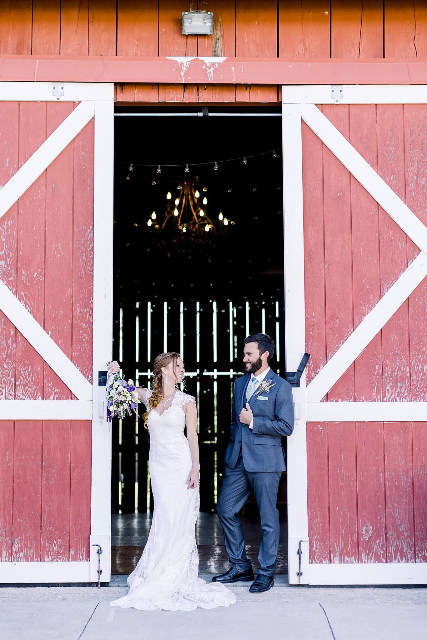 Bride and groom pose with red barn doors during Crooked Creek Ranch wedding.