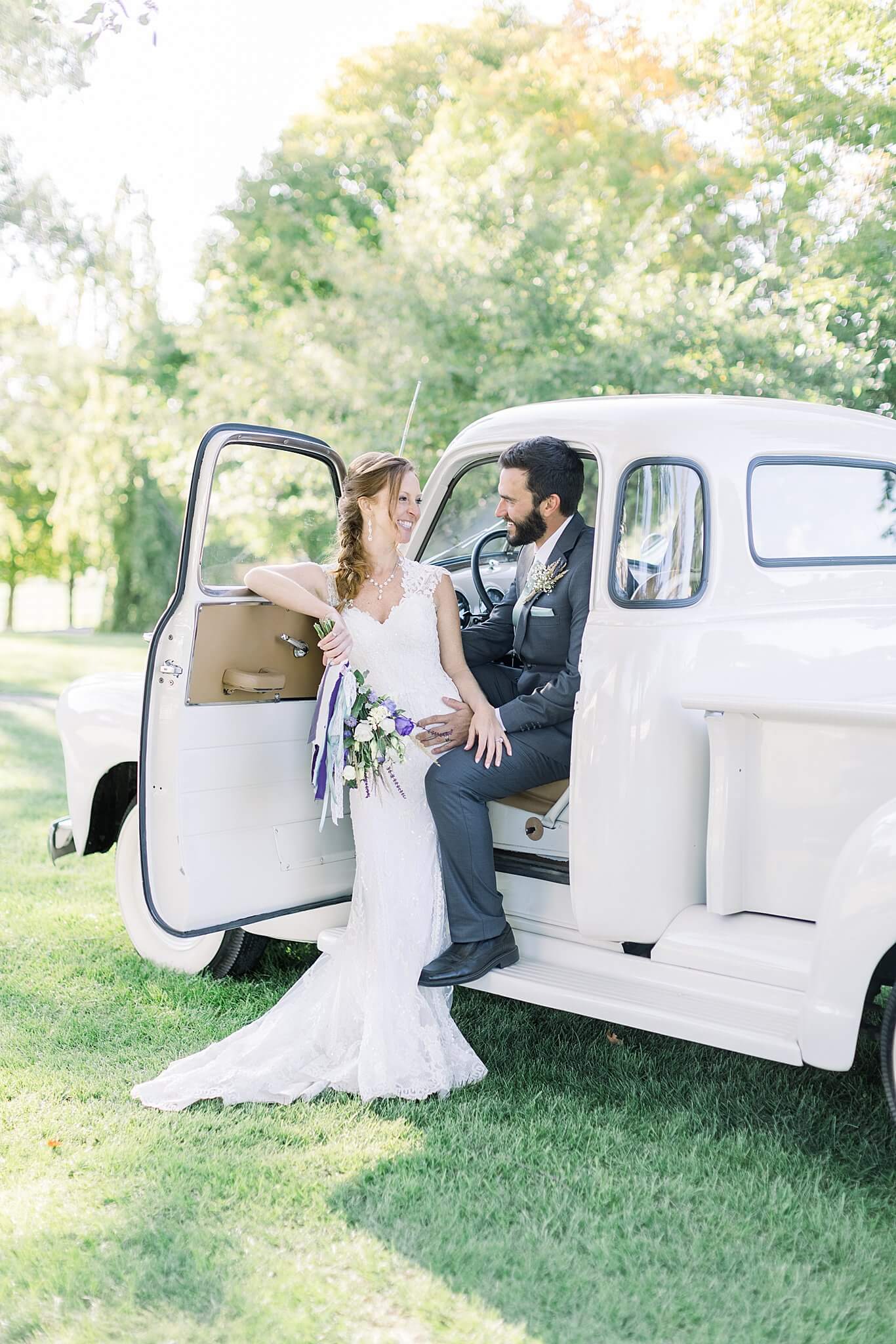 Bride smiles at groom in vintage, white Chevy truck during Crooked Creek Ranch wedding.