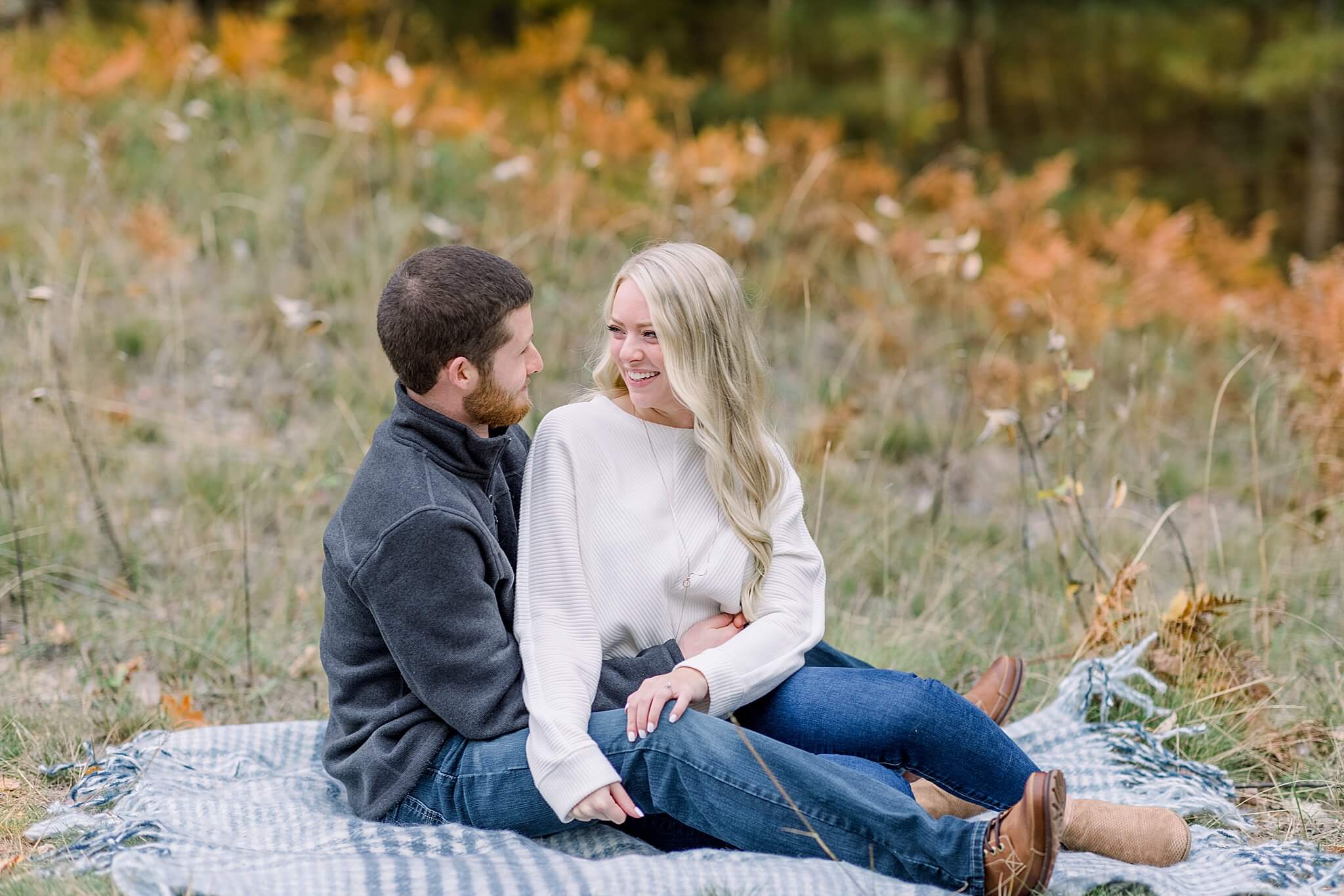 Bride and groom snuggle surrounded by fall colors during M22 Fall Engagement Session in Northern Michigan.