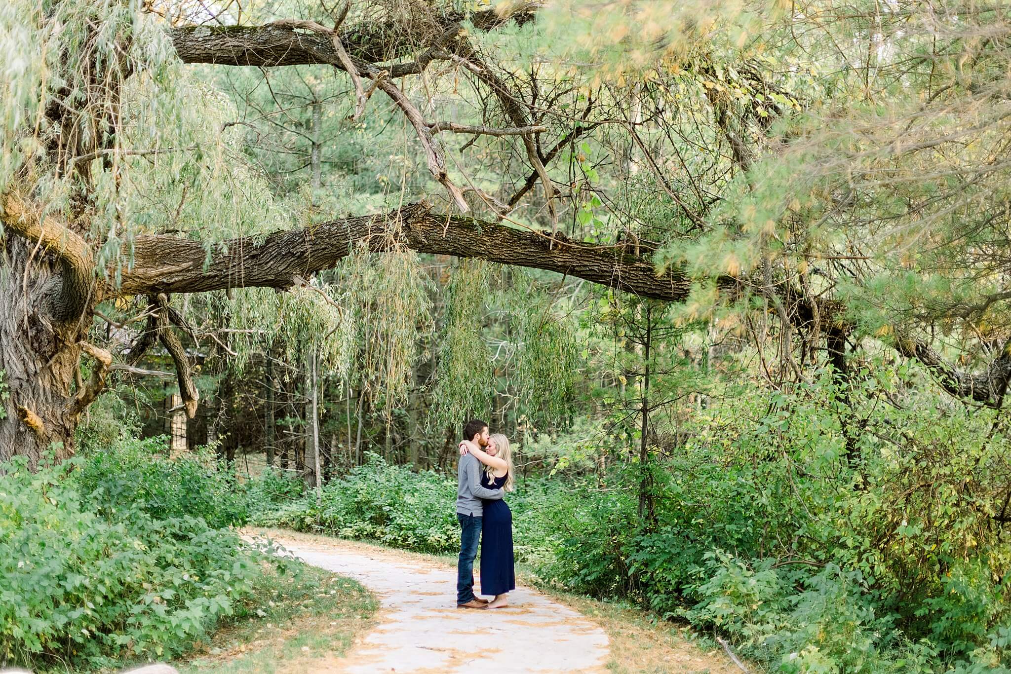 Bride and groom kiss on moss lined path during M22 Fall Engagement Session in Northern Michigan.