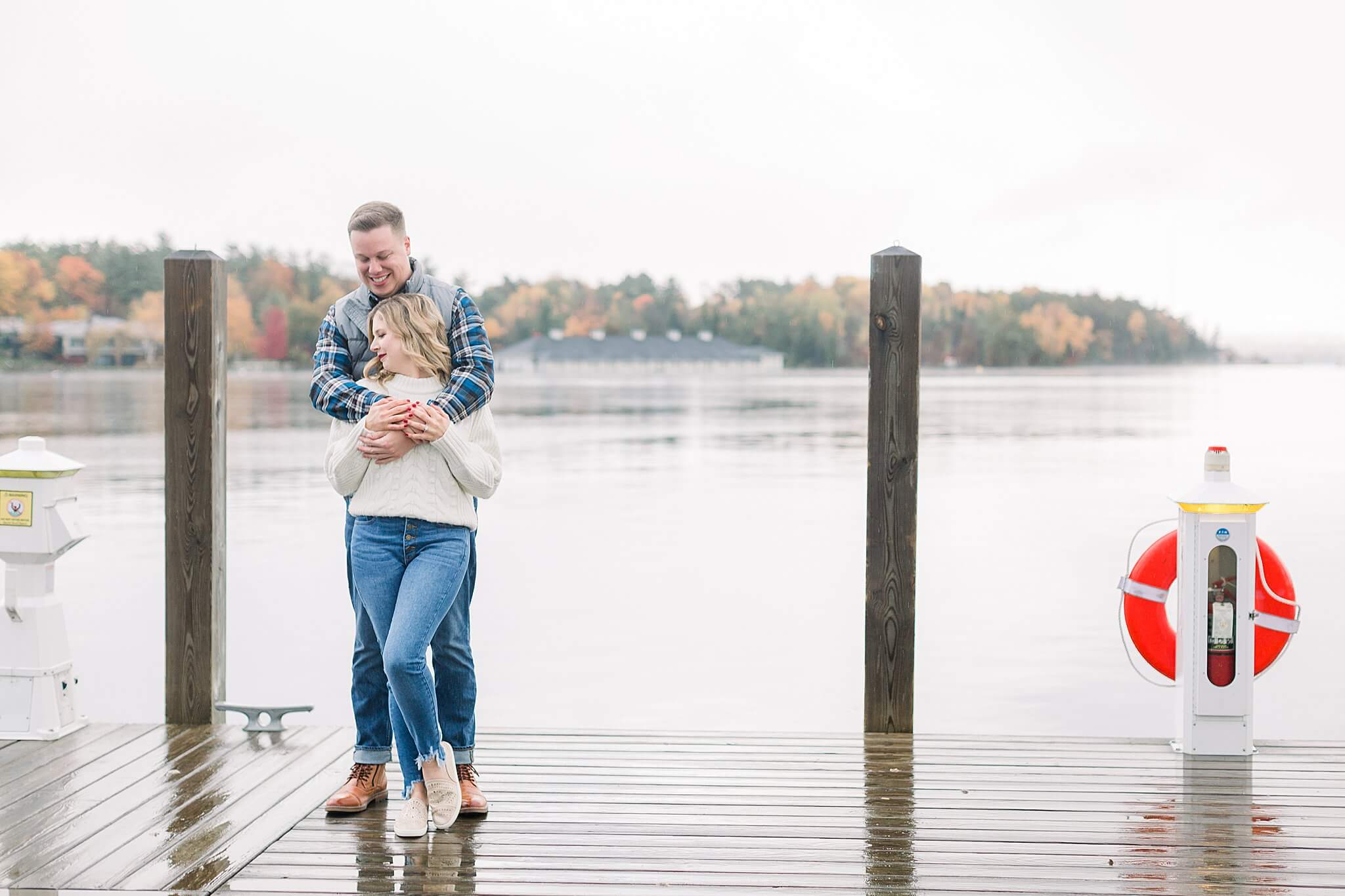 Bride and groom snuggle on dock during rainy fall engagement session in Charlevoix, Michigan.