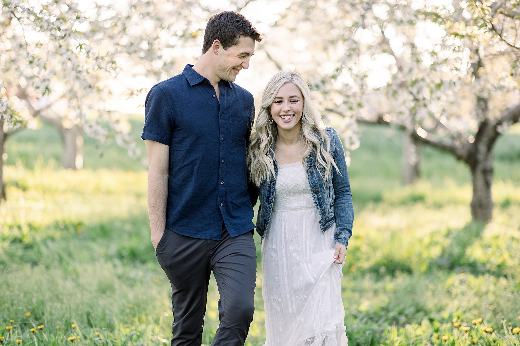 Couple laughs while walking through Traverse City cherry orchard their cherry blossom engagement session in Northern Michigan. 