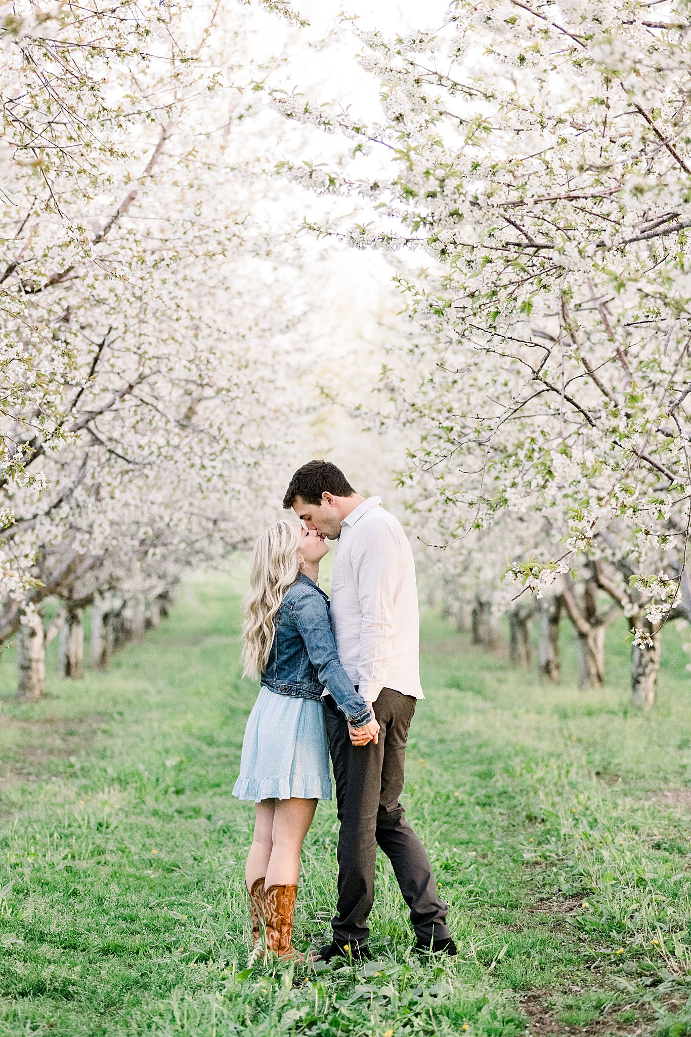 Couple kissing during engagement session among the gorgeous cherry blossom blooms during their Traverse City engagement session in Northern Michigan.