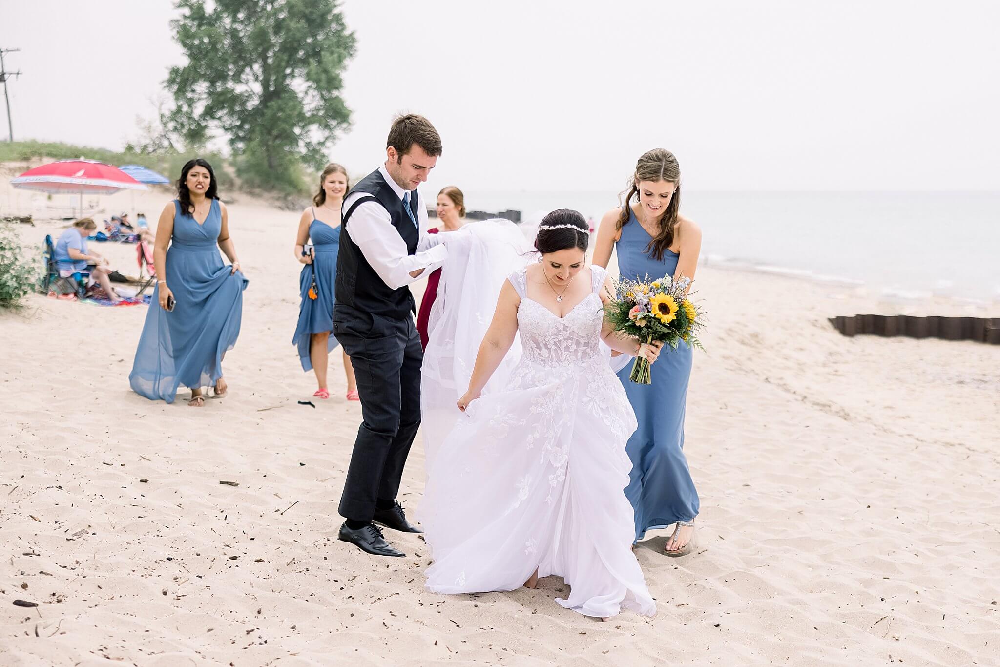 Bridal party helps bride make her way to the groom on the beach before their Elberta Life Saving Station wedding day.