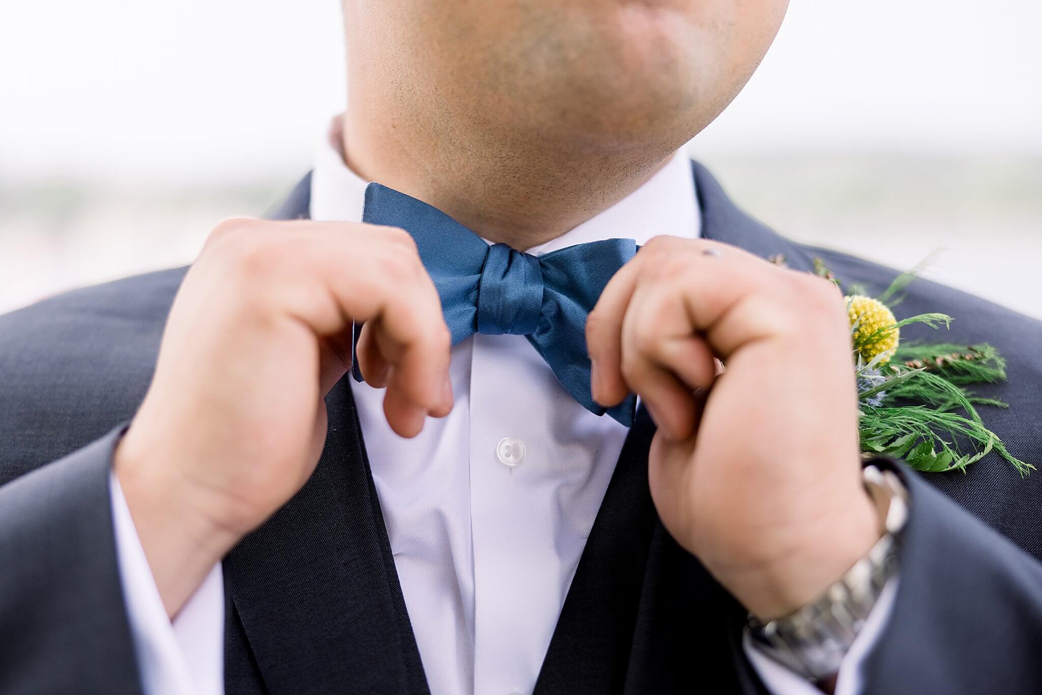 Groom adjusts bow tie during Elberta Life Saving Station wedding day.