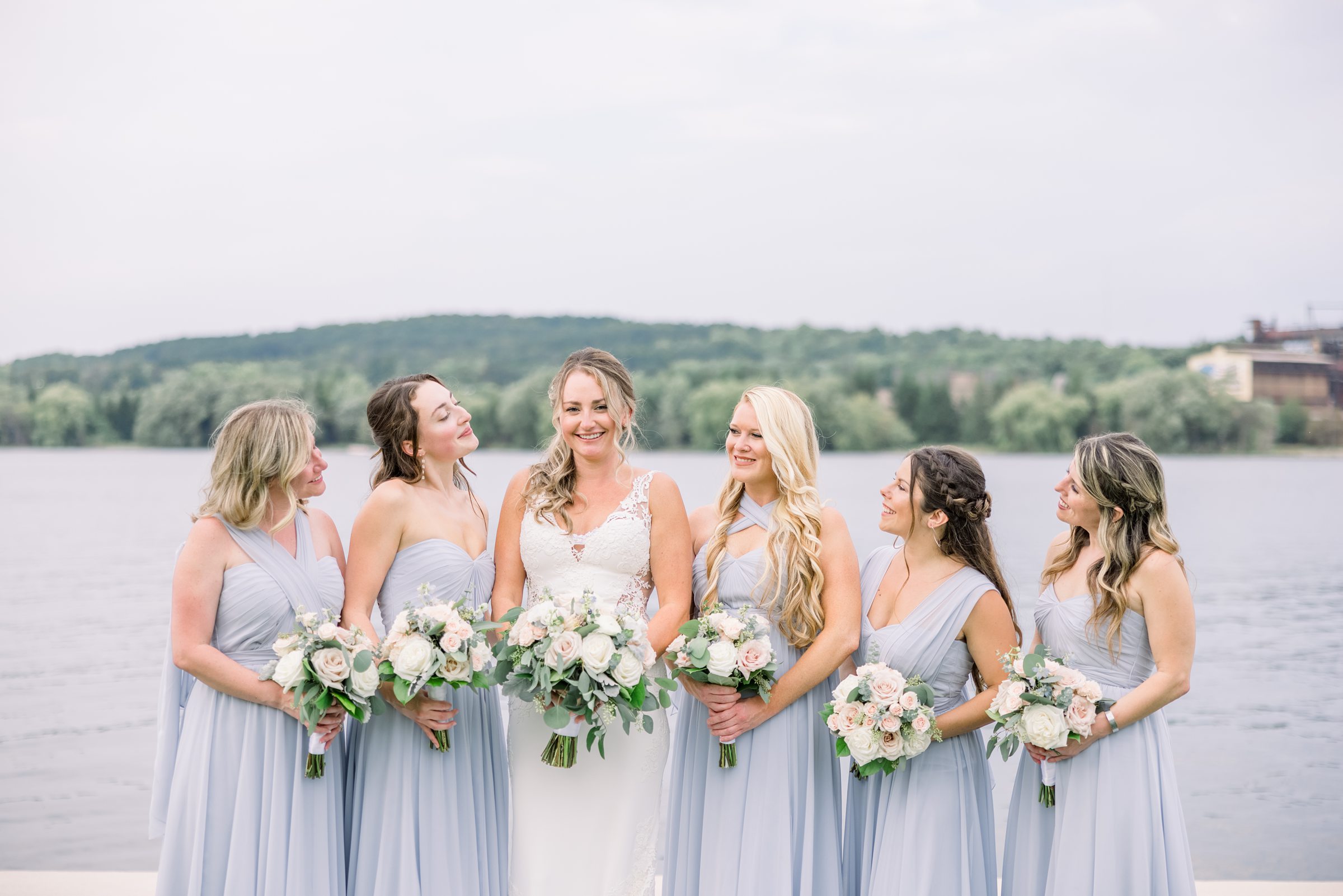 Bridesmaids smile at bride during her wedding on the Lake Charlevoix shore.