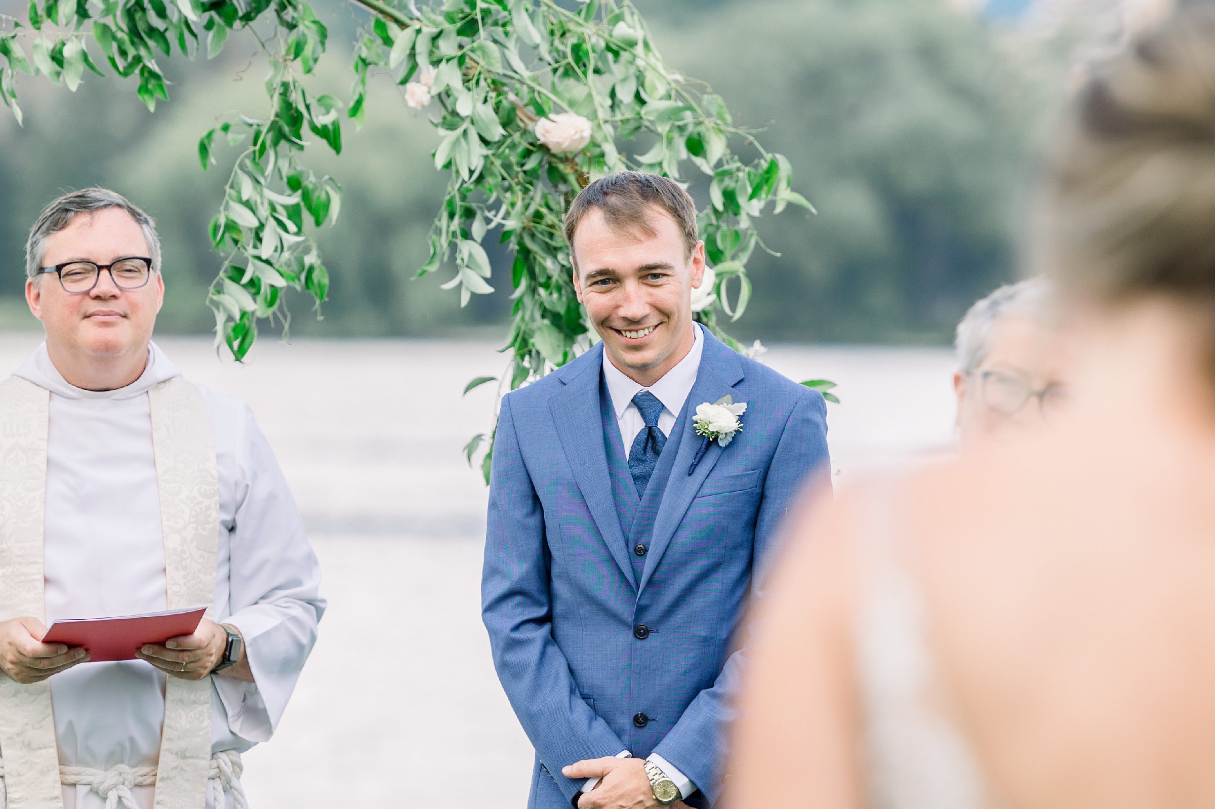 Groom smiles at bride as she walks down the aisle during Boathouse on Lake Charlevoix wedding