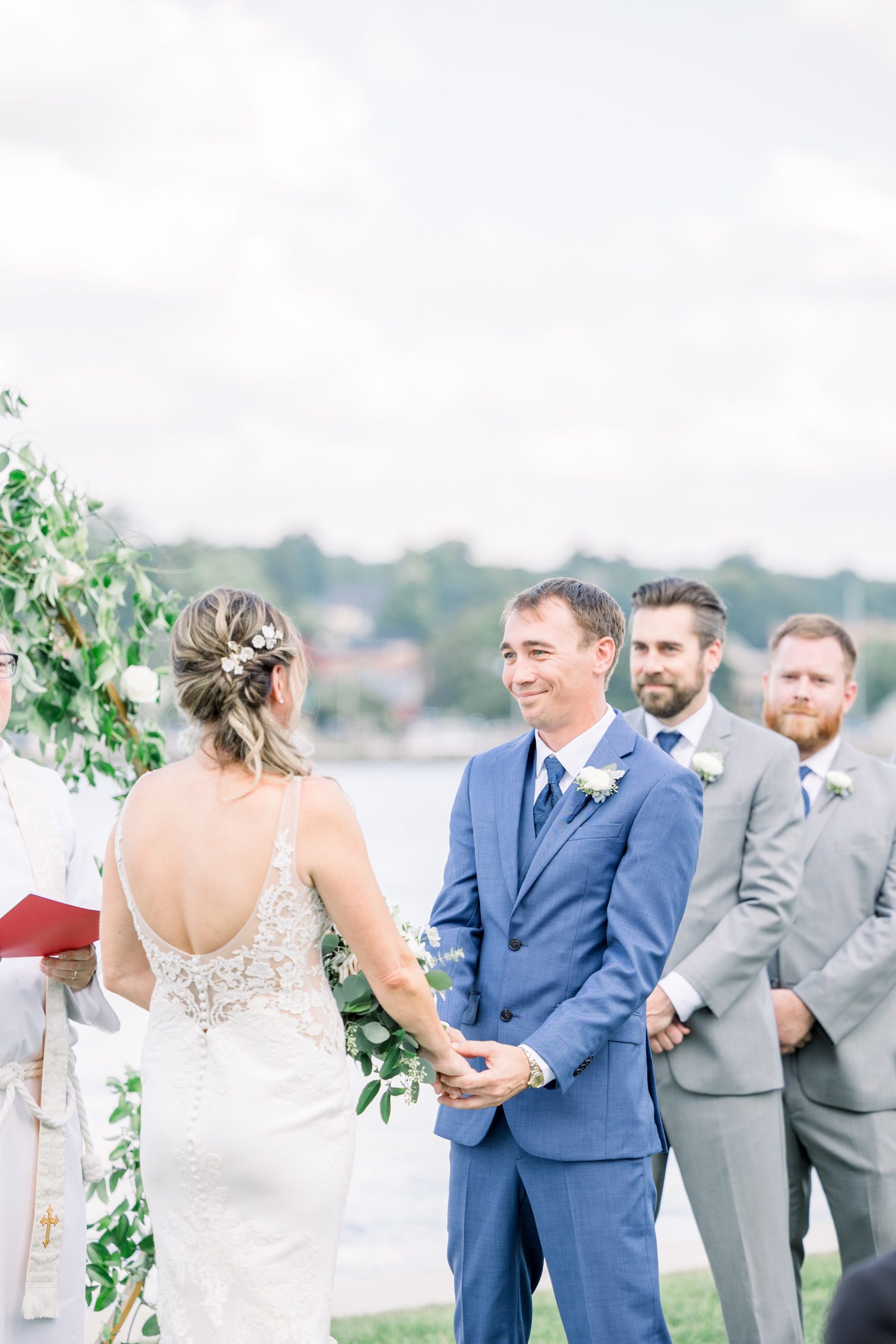 Groom smiles at bride during wedding ceremony at The Boathouse on Lake Charlevoix.
