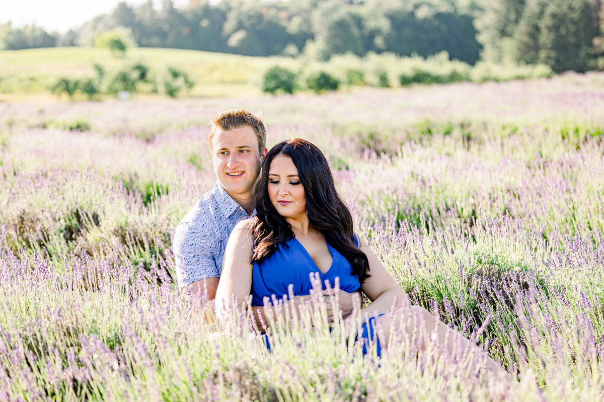 Lindsey and Austin looking off in the distance as they sit together in a lavender field during their engagement session with Mandie Forbes Photography.