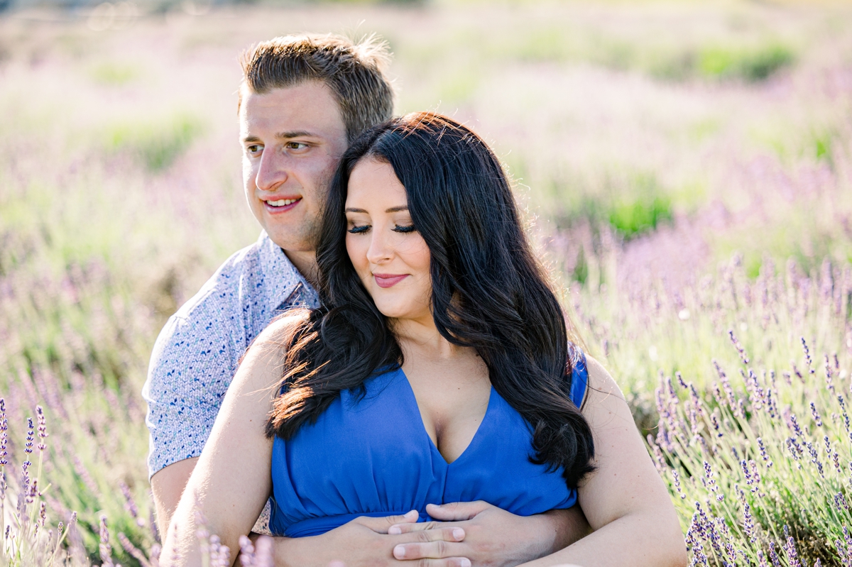 Lindsey and Austin looking off in the distance as they sit together in a lavender field during their engagement session with Mandie Forbes Photography.