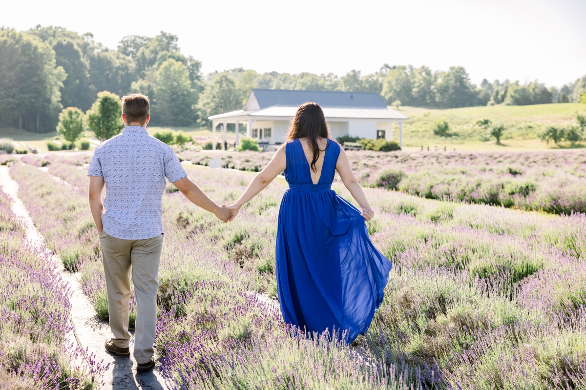 Lindsey and Austin walking hand in hand away from the camera through a lavender field.