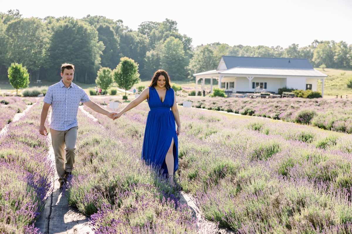 Lindsey and Austin walking hand in hand through a lavender field during their engagement session with Mandie Forbes Photography.