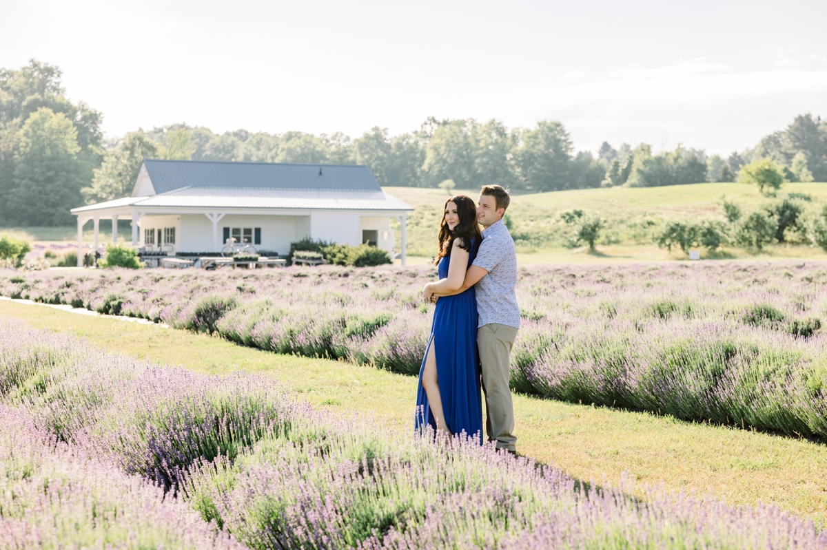 Austin hugging Lindsey from behind in the middle of a lavender field during their engagement session with Mandie Forbes Photography.