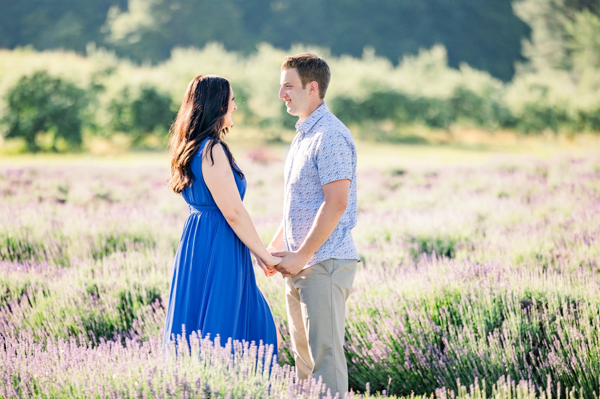 Lindsey and Austin holding hands while they smile at each other in a lavender field.