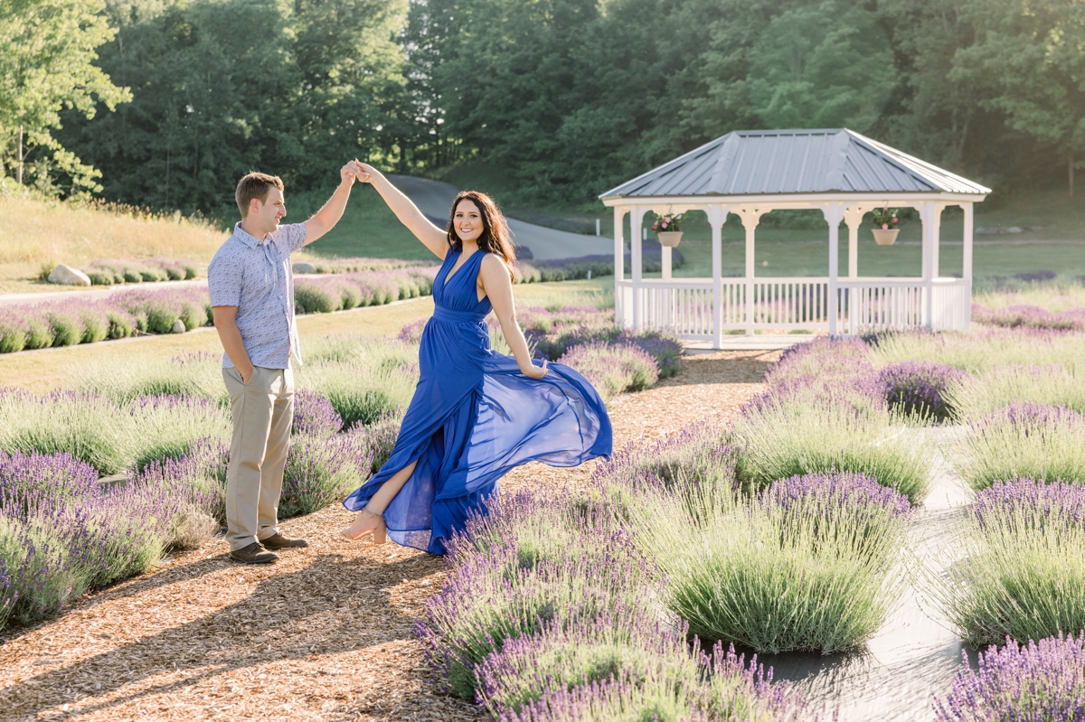 Austin spinning Lindsey around while she plays with the skirt of her dress in a lavender field during their engagement session.