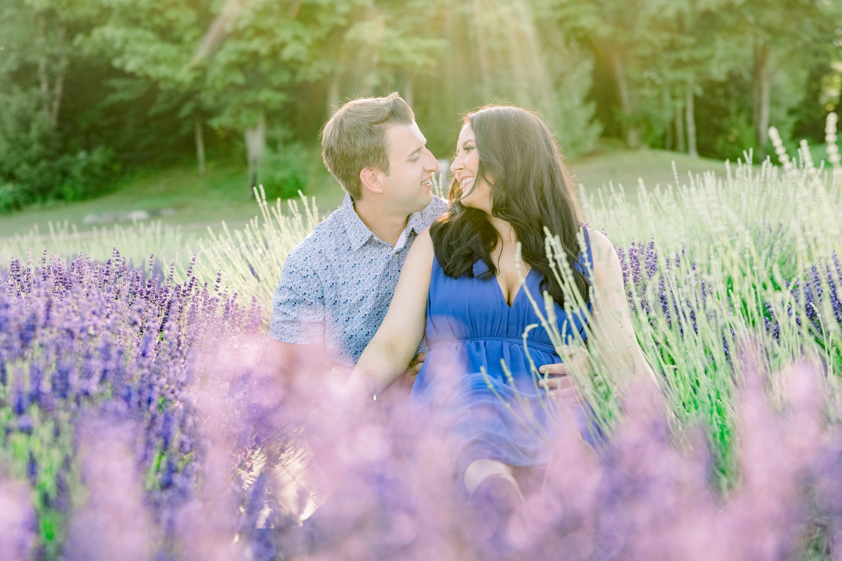 Lindsey and Austin sitting in a lavender field smiling at each other during their engagement session with Mandie Forbes Photography.