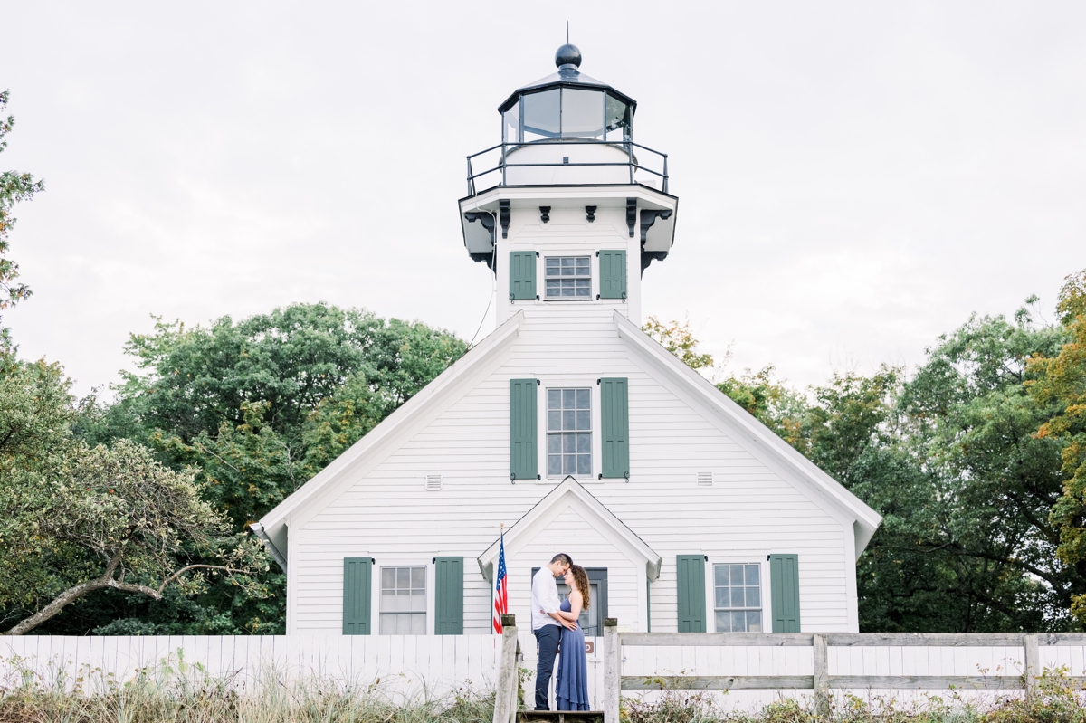 Marissa and Alex smiling in front of a lighthouse during their engagement session.