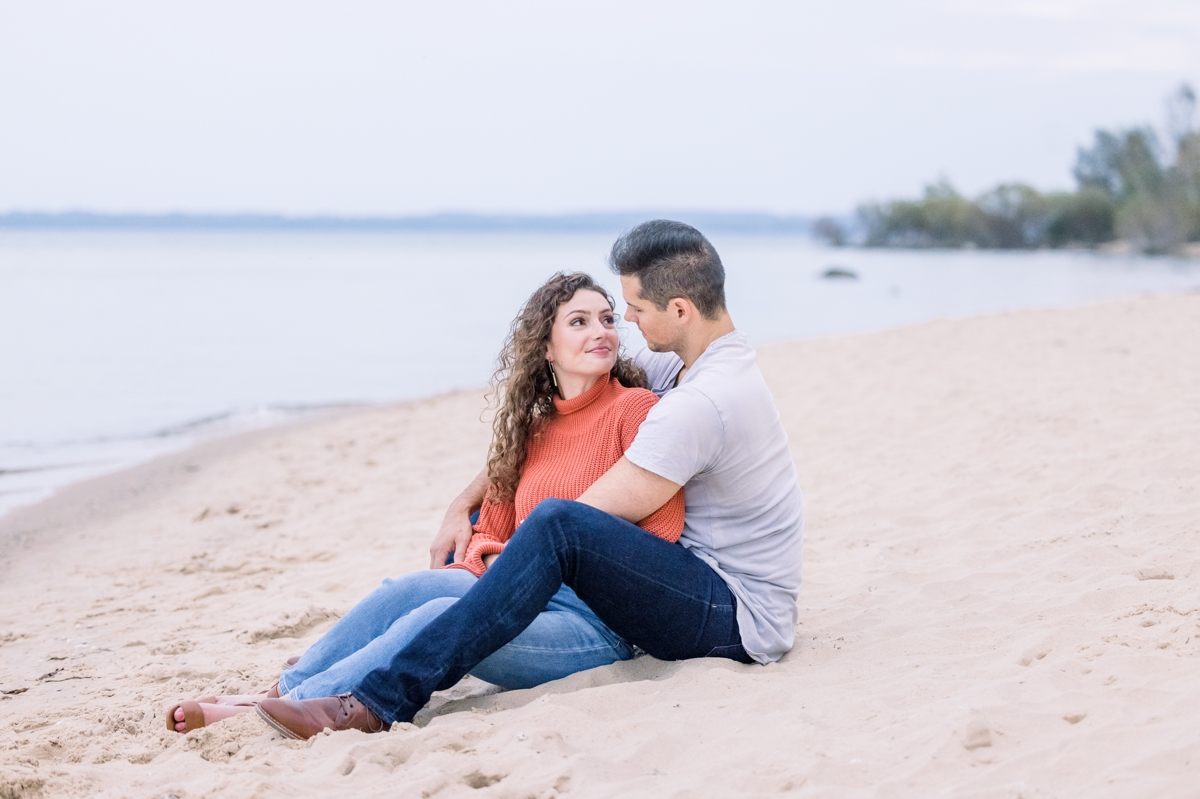 Marissa and Alex sitting in the sand looking at each other during their beach engagement session.