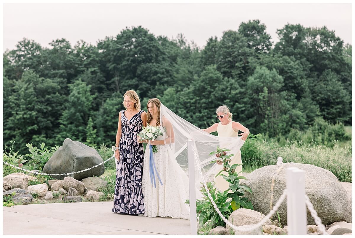 A bride prepares to walk down the aisle with her mother at her emotional Bay View wedding day ceremony. Her wedding planner is straightening the bride's veil before she takes her first step down the aisle.