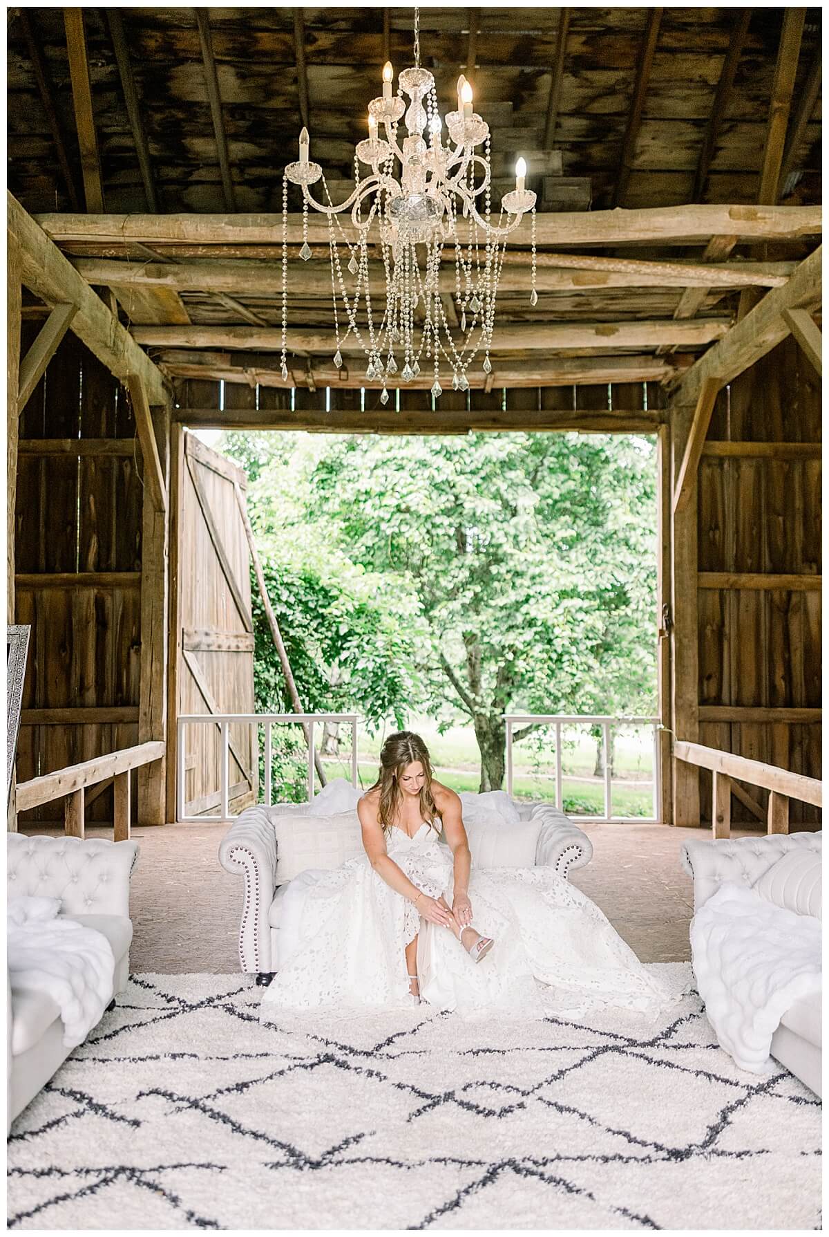 Bride lacing up her shoes under a chandelier at the getting ready barn located at Bay View weddings in Traverse City, Michigan.