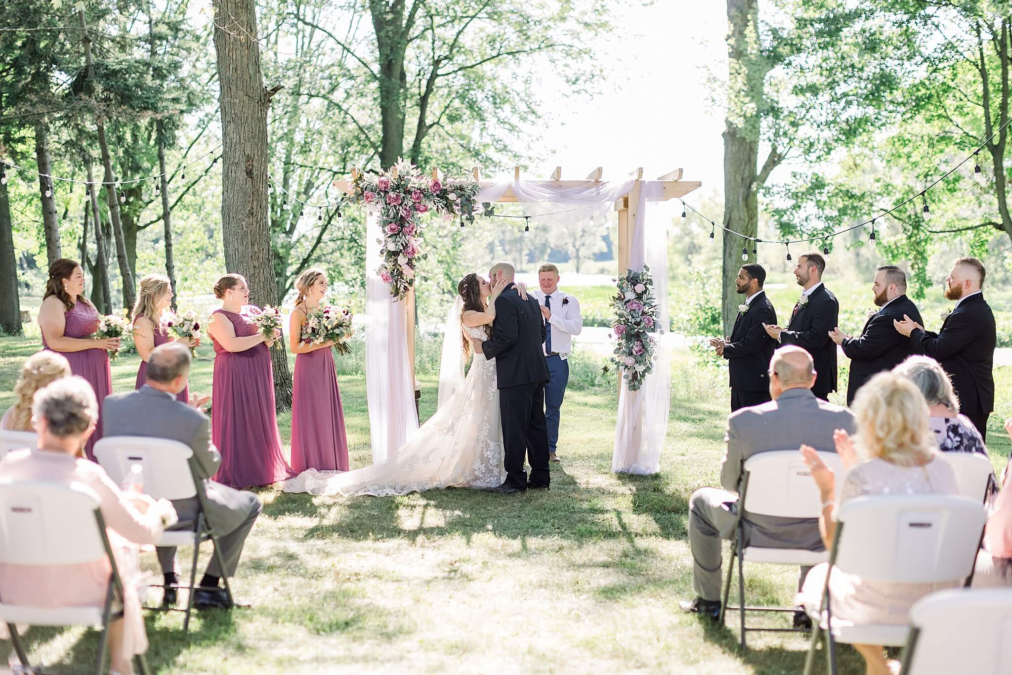 Bride and groom share first kiss during Michigan Summer Backyard Wedding ceremony.