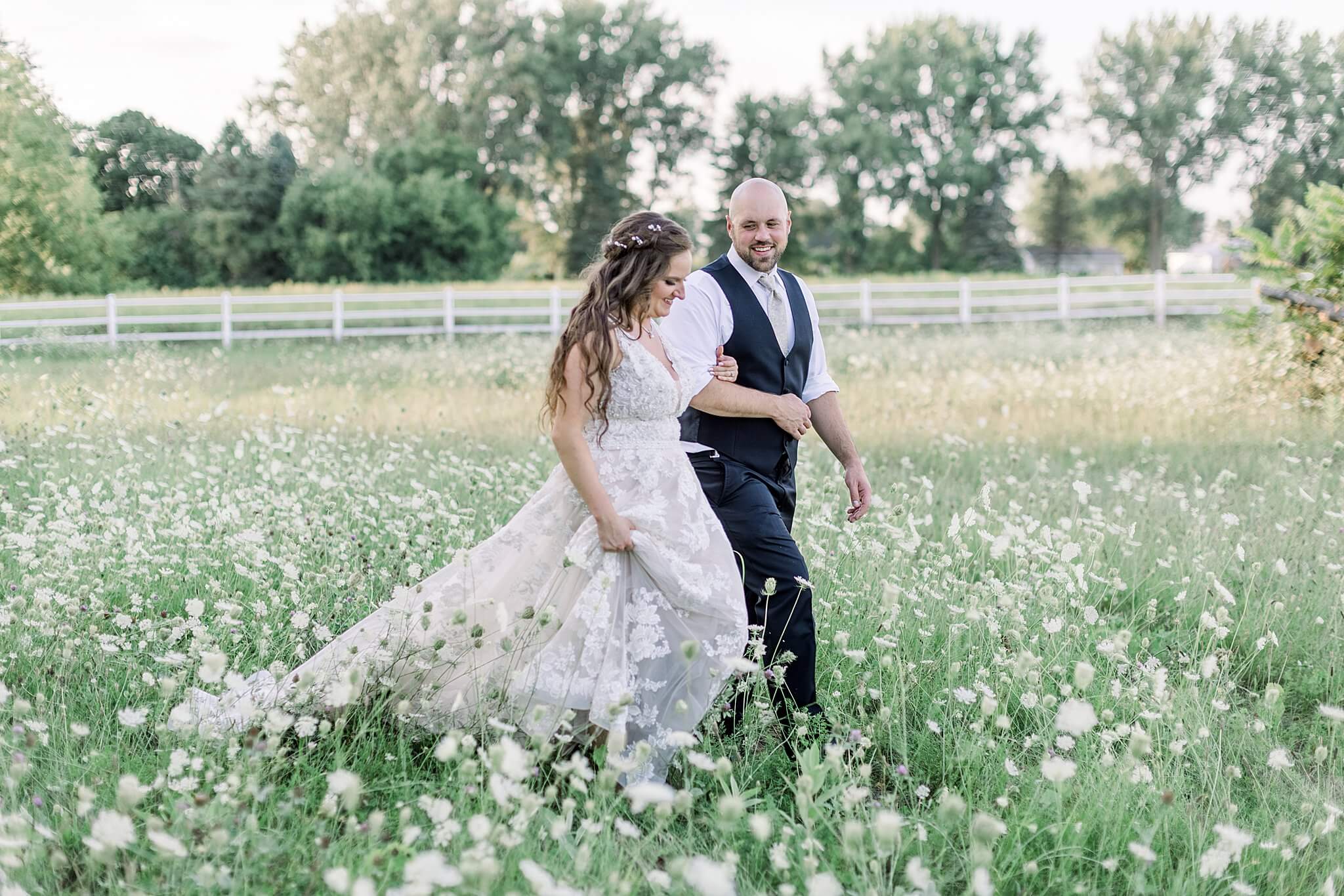 Bride and groom walk through field of queen's anne lace during Michigan Summer Backyard Wedding