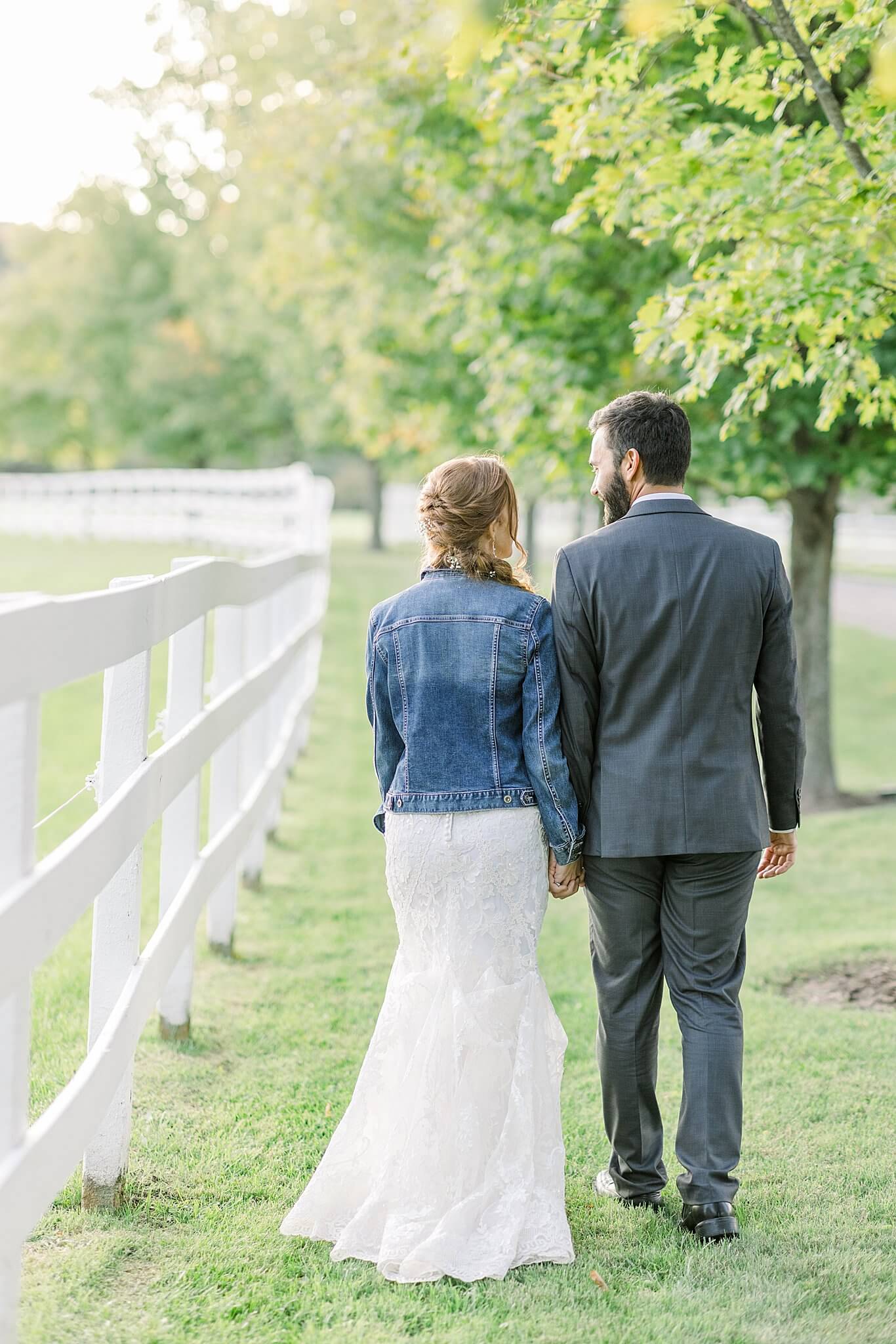 Bride and groom walk along white picket fence during Crooked Creek Ranch wedding.