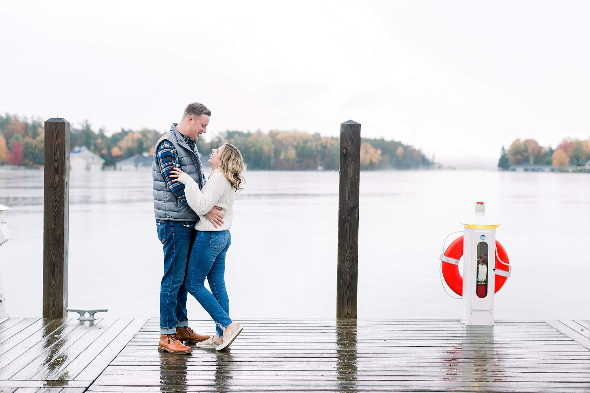 Bride smiles at groom during rainy fall engagement session in Charlevoix, Michigan.