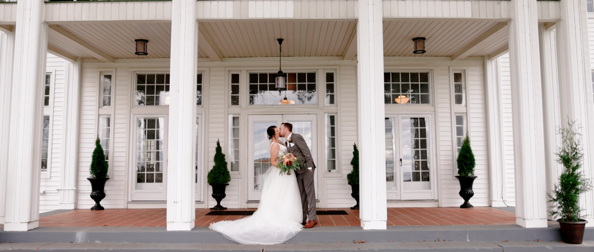 Bride and groom kiss under the columns on the front porch during their Waldenwoods wedding in Howell, Michigan.