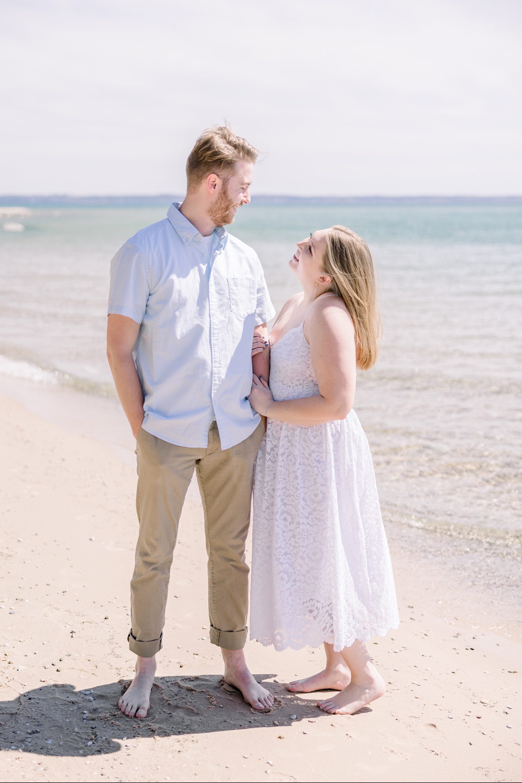 Couple smiles at each other on beach during Harbor Springs engagement session. 